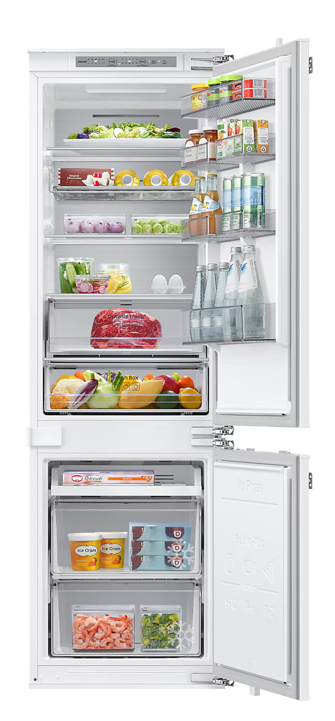 Biała lodówka, otwarta, z półkami pełnymi jedzenia: warzywa, napoje i jajka.