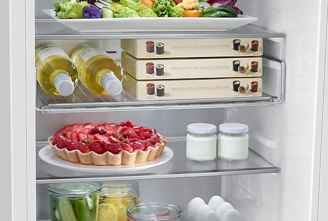 Wnętrze lodówki, otwarte. Półki z butelkami wina, ciastem i czekoladą.