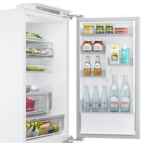 Otwarta biała lodówka z półkami pełnymi jedzenia: butelki, słoiki i świeże produkty.