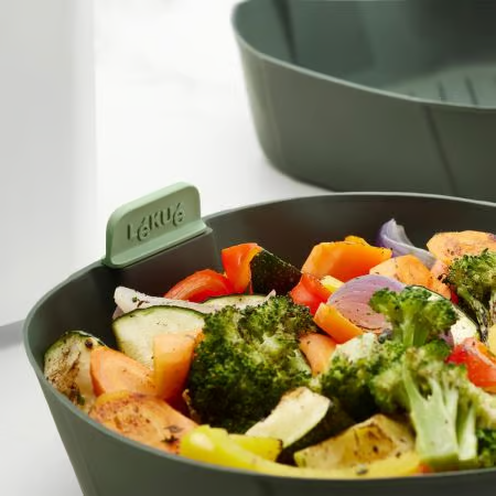 Nahaufnahme von gekochtem Gemüse in einem grünen Behälter. Enthält Brokkoli, Karotten und Zucchini.