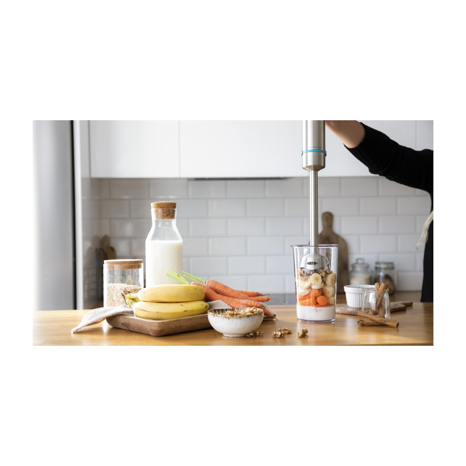 Una persona frulla frutta e verdura con un frullatore a immersione. Ingredienti: carote, banane e latte.