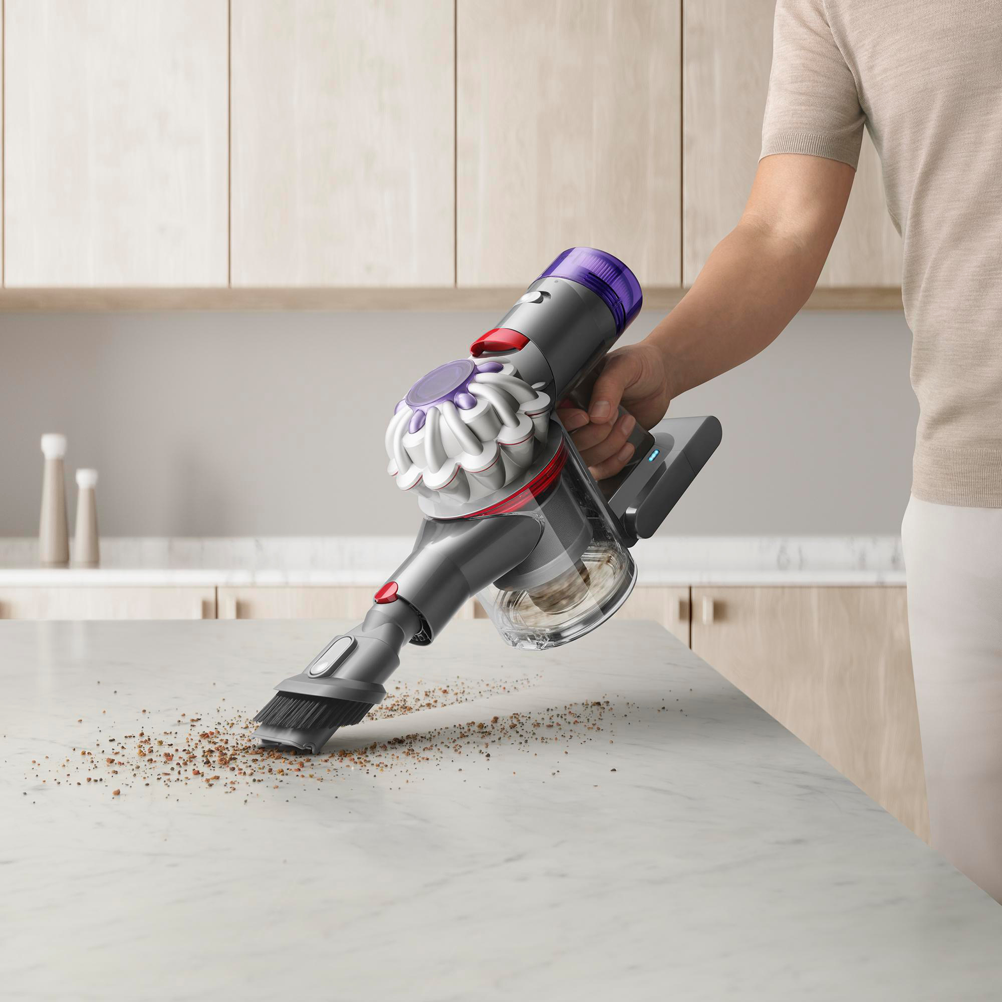 Eine Hand saugt eine weiße Arbeitsplatte. Der Staubsauger ist grau, lila und rot. Auf der Theke sind Ablagerungen zu sehen.