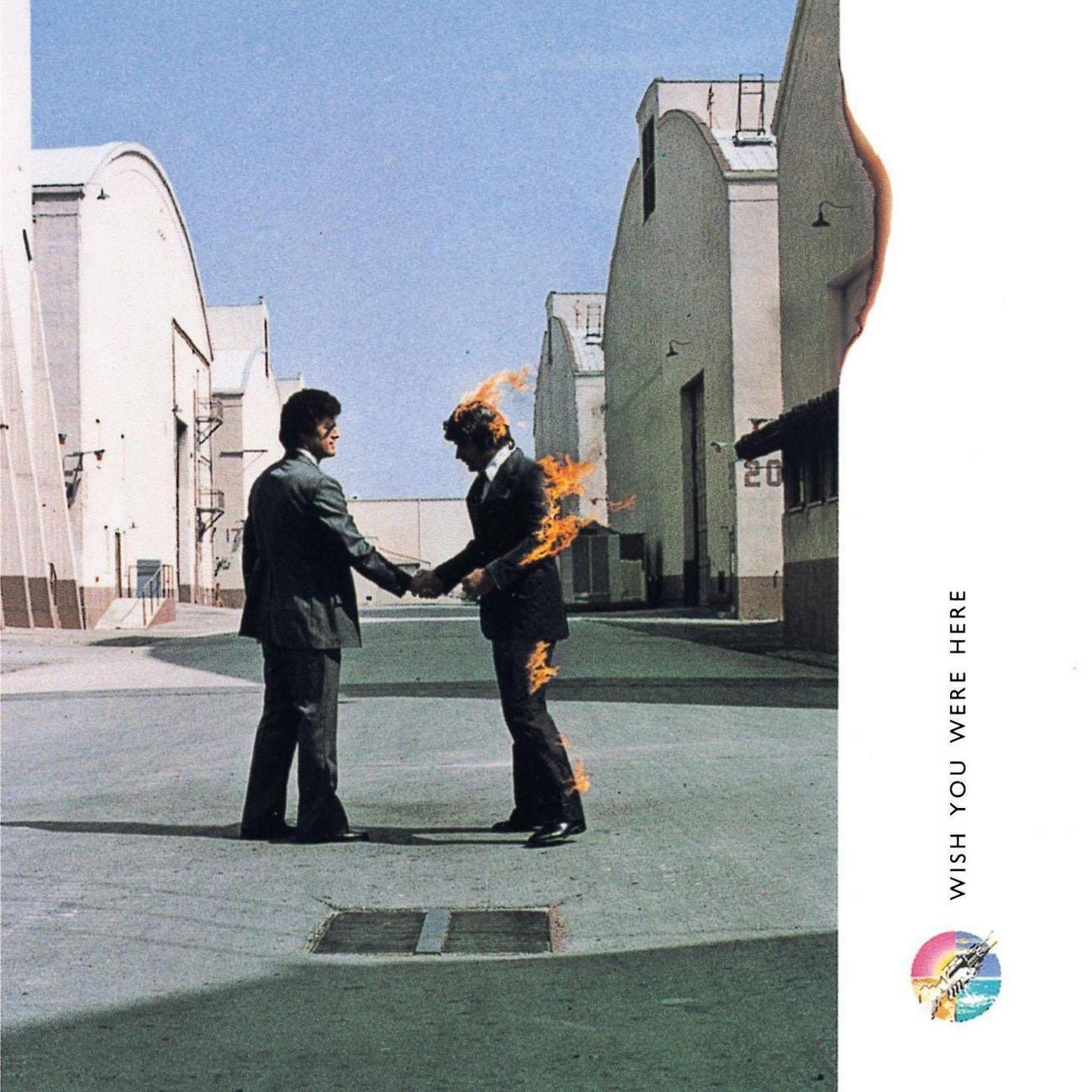 Zwei Männer geben sich die Hand, einer steht in Flammen, vor weißen Gebäuden. Albumcover.
