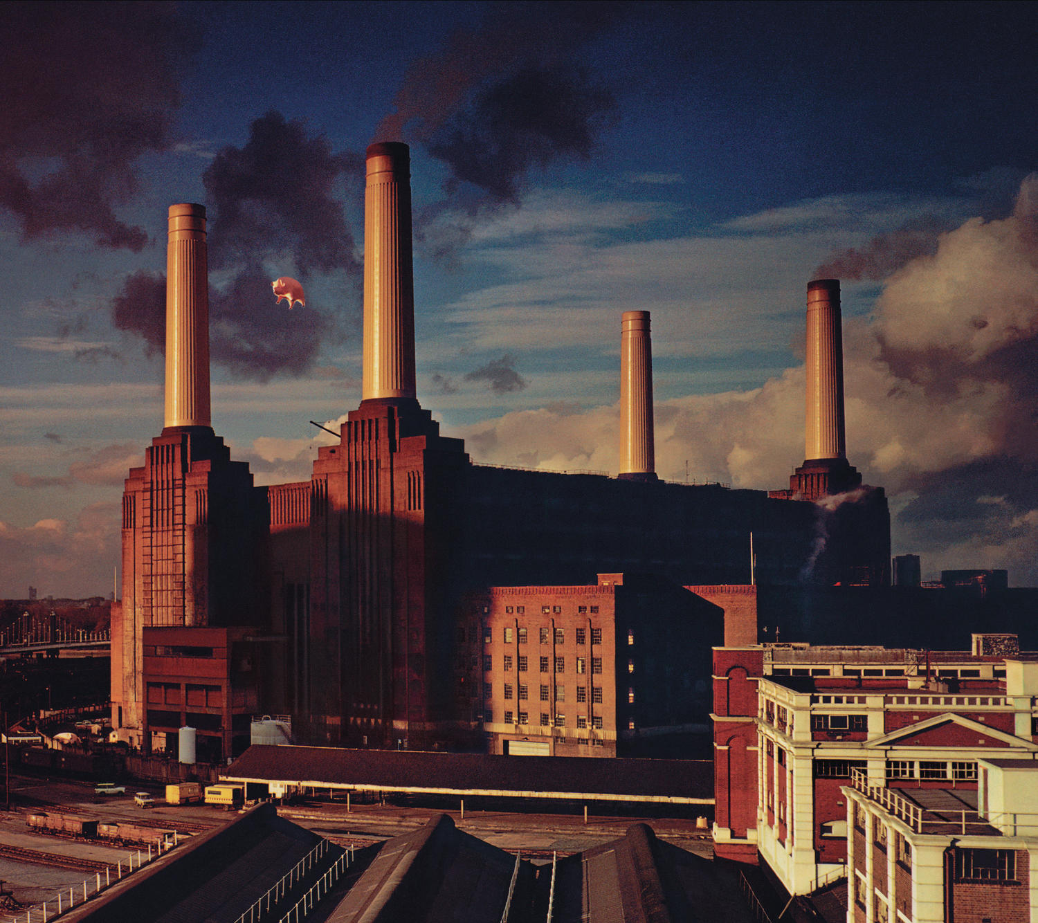 Pink Floyds Albumcover. Großes Industriegebäude mit Schornsteinen. Ein rosa Schwein schwebt am Himmel.