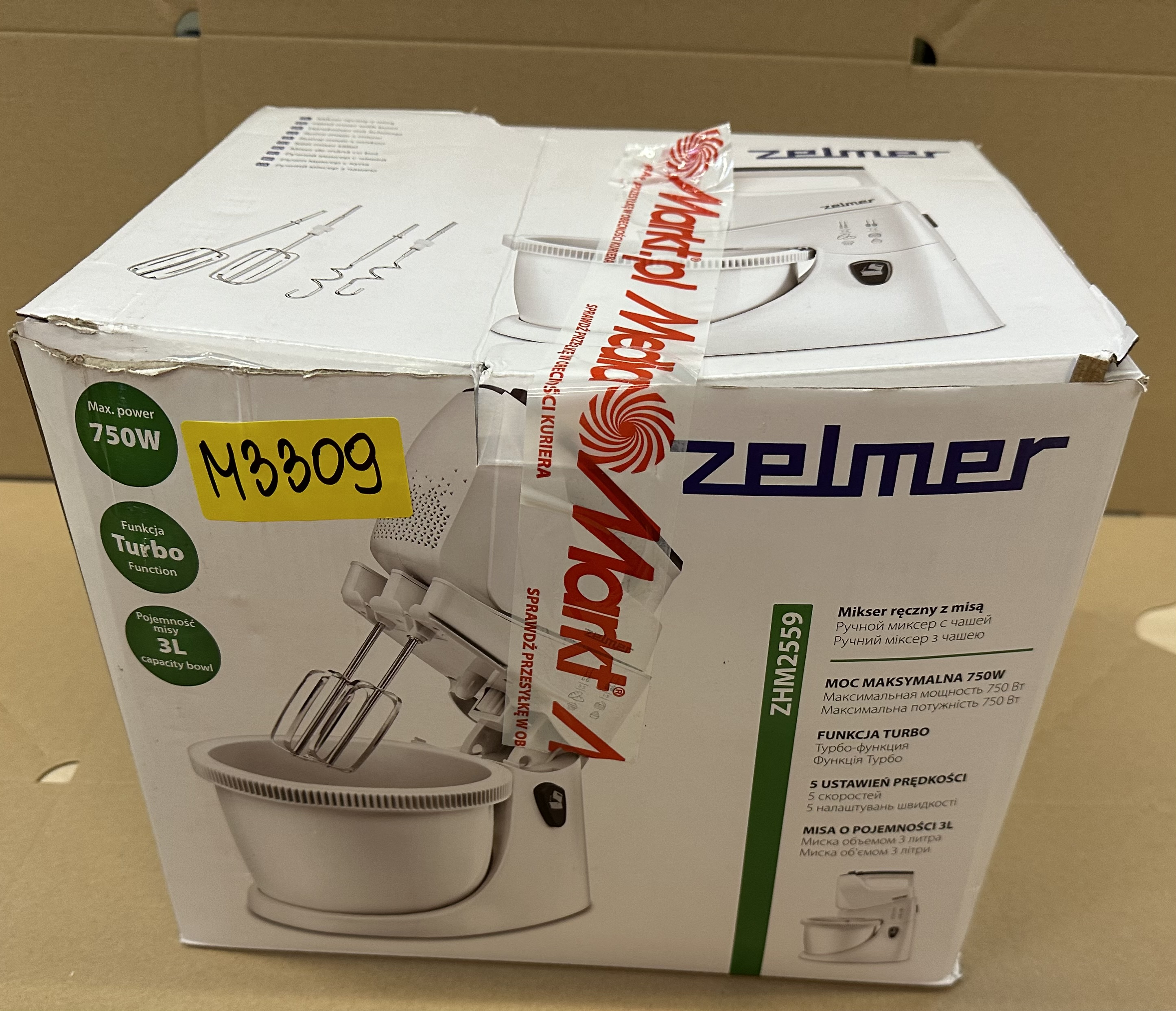 Zapakowane białe urządzenie kuchenne, z dołączonym mikserem, z etykietami i taśmą.