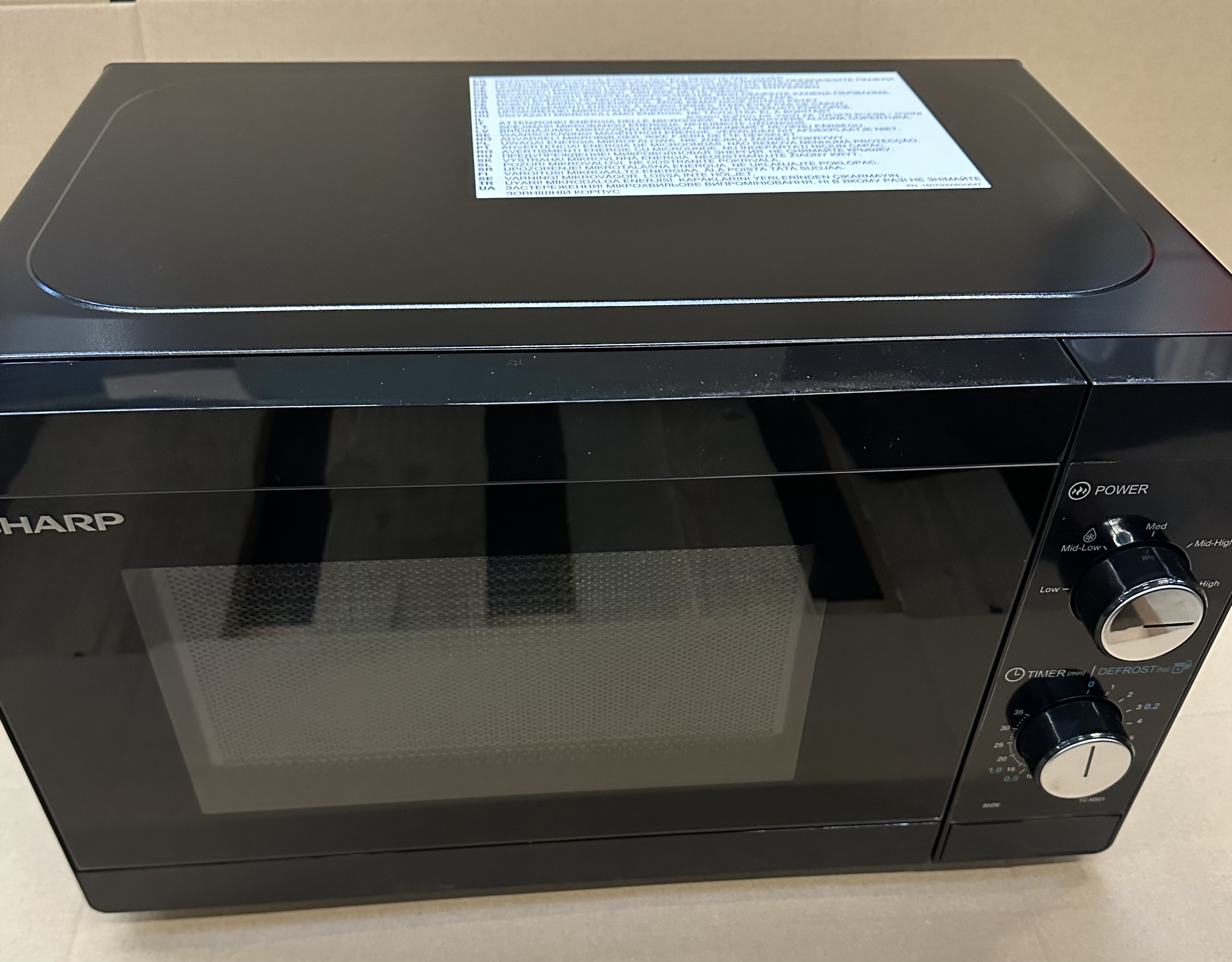Czarna kuchenka mikrofalowa Sharp z pokrętłami sterującymi i timerem.