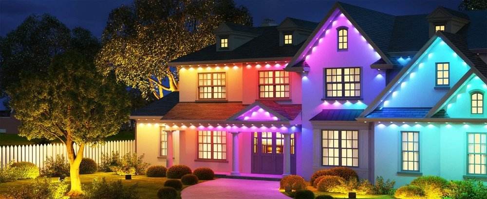 Zewnętrze domu w nocy, udekorowane kolorowymi inteligentnymi światłami. Drzewa, trawnik i niebo.