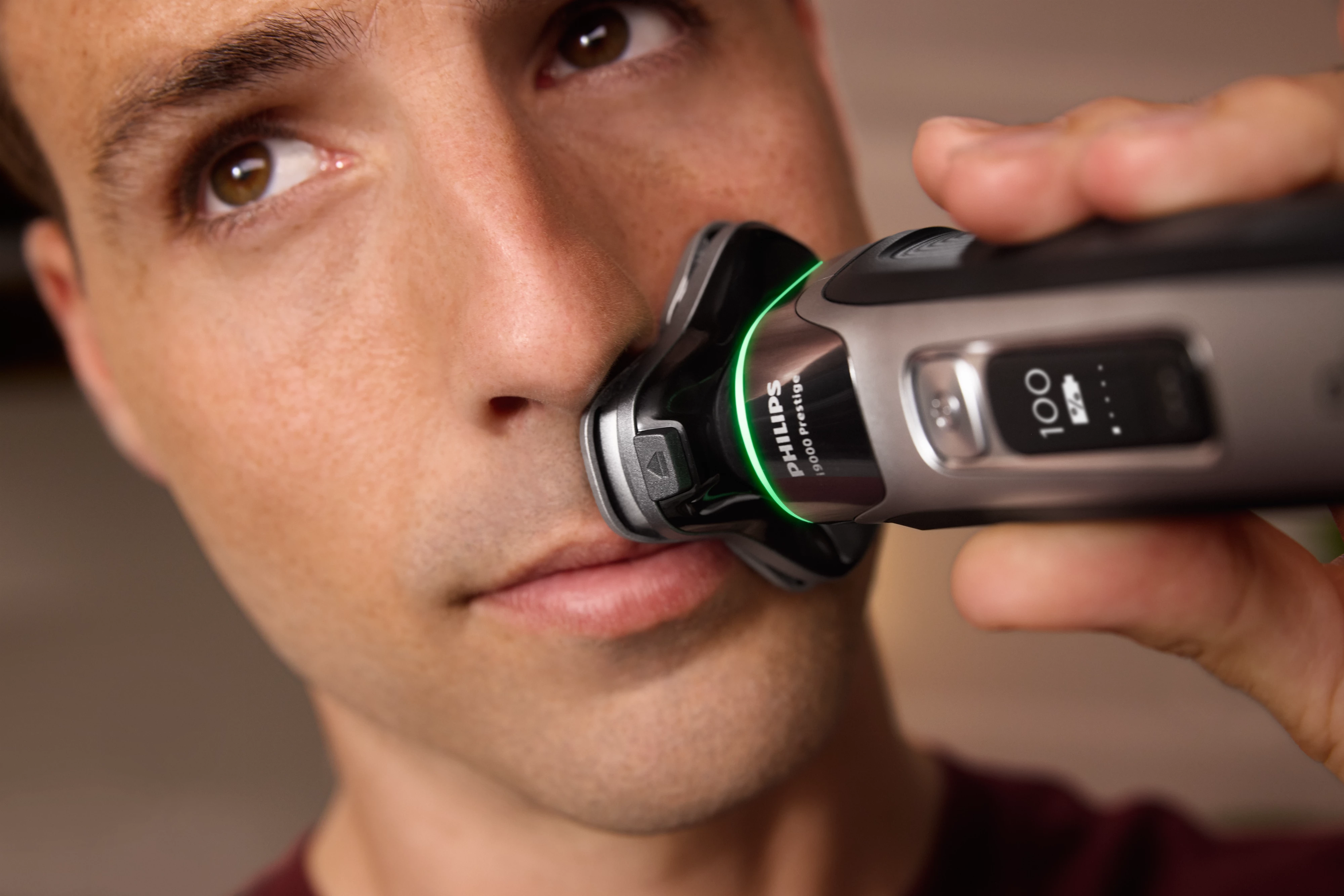Un uomo che si rade la faccia con un rasoio elettrico Philips nero e argento.