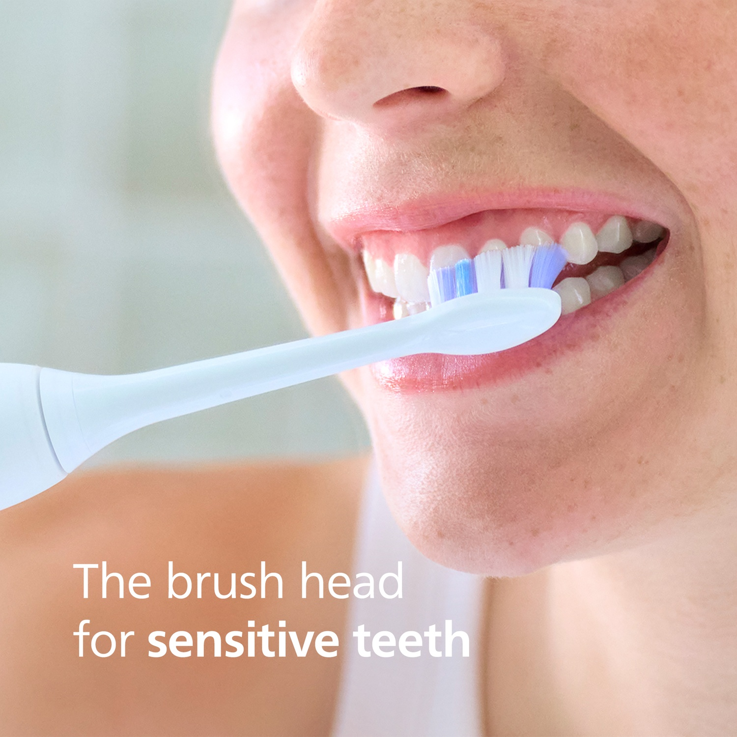 A woman brushes her teeth with a white electric toothbrush. Her mouth is open.