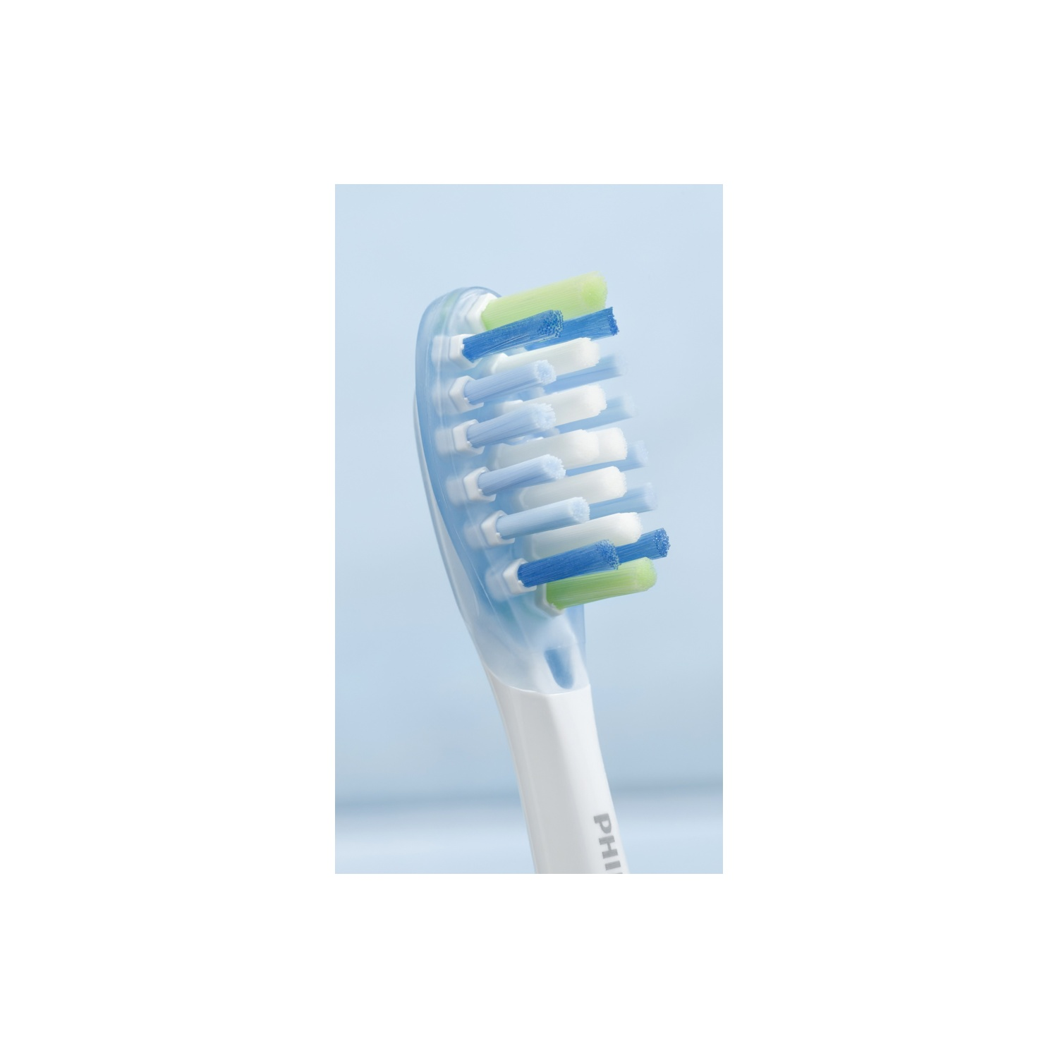 Gros plan d'une tête de brosse à dents avec des poils blancs, bleus et verts. Le manche est blanc et transparent.