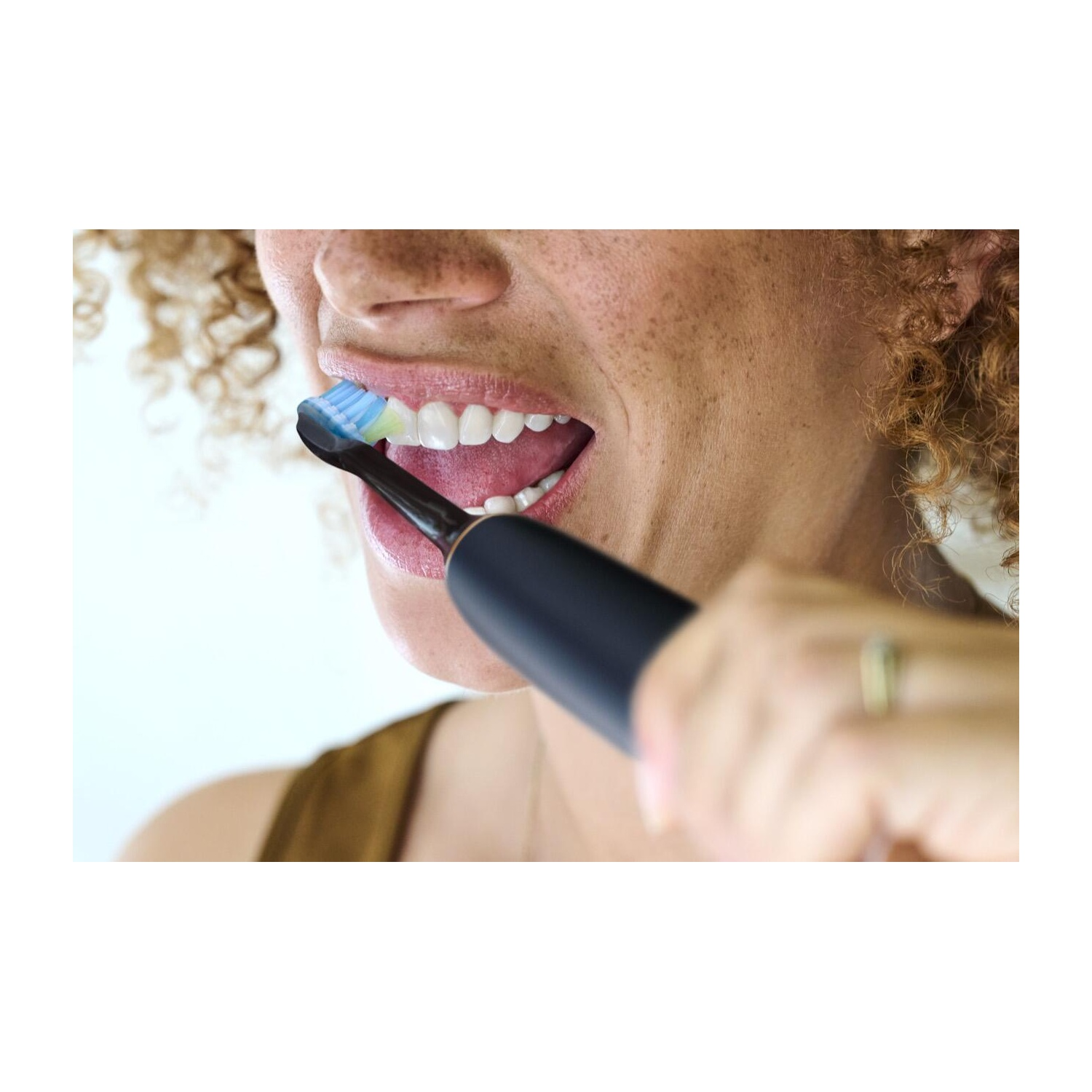 Woman brushing her teeth with a black toothbrush. Her mouth is open, showing teeth.