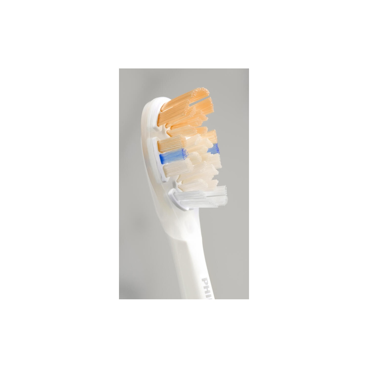 Gros plan sur une tête de brosse à dents blanche avec des poils orange, blancs et bleus. Fond gris.