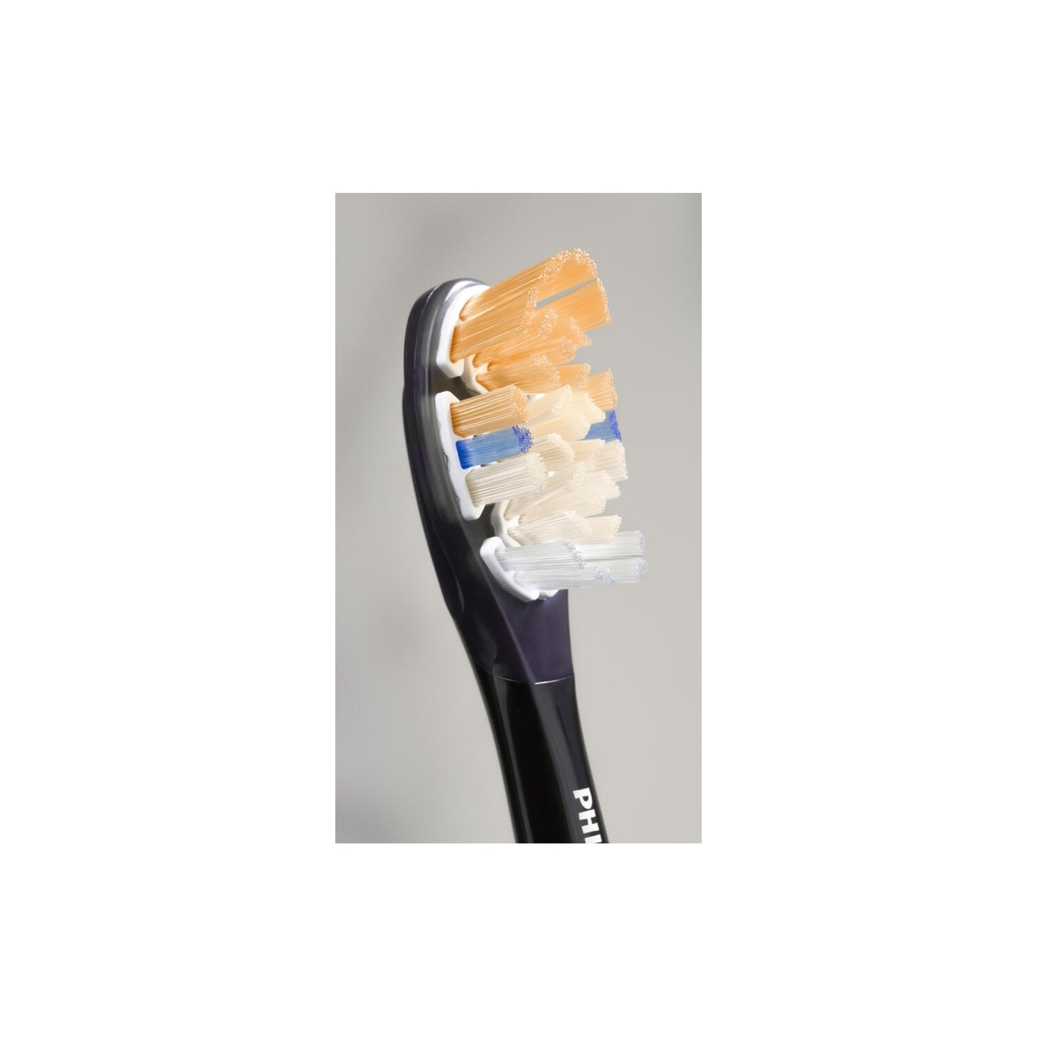 Close-up of a white toothbrush head with orange, white, and blue bristles. Dark blue handle.