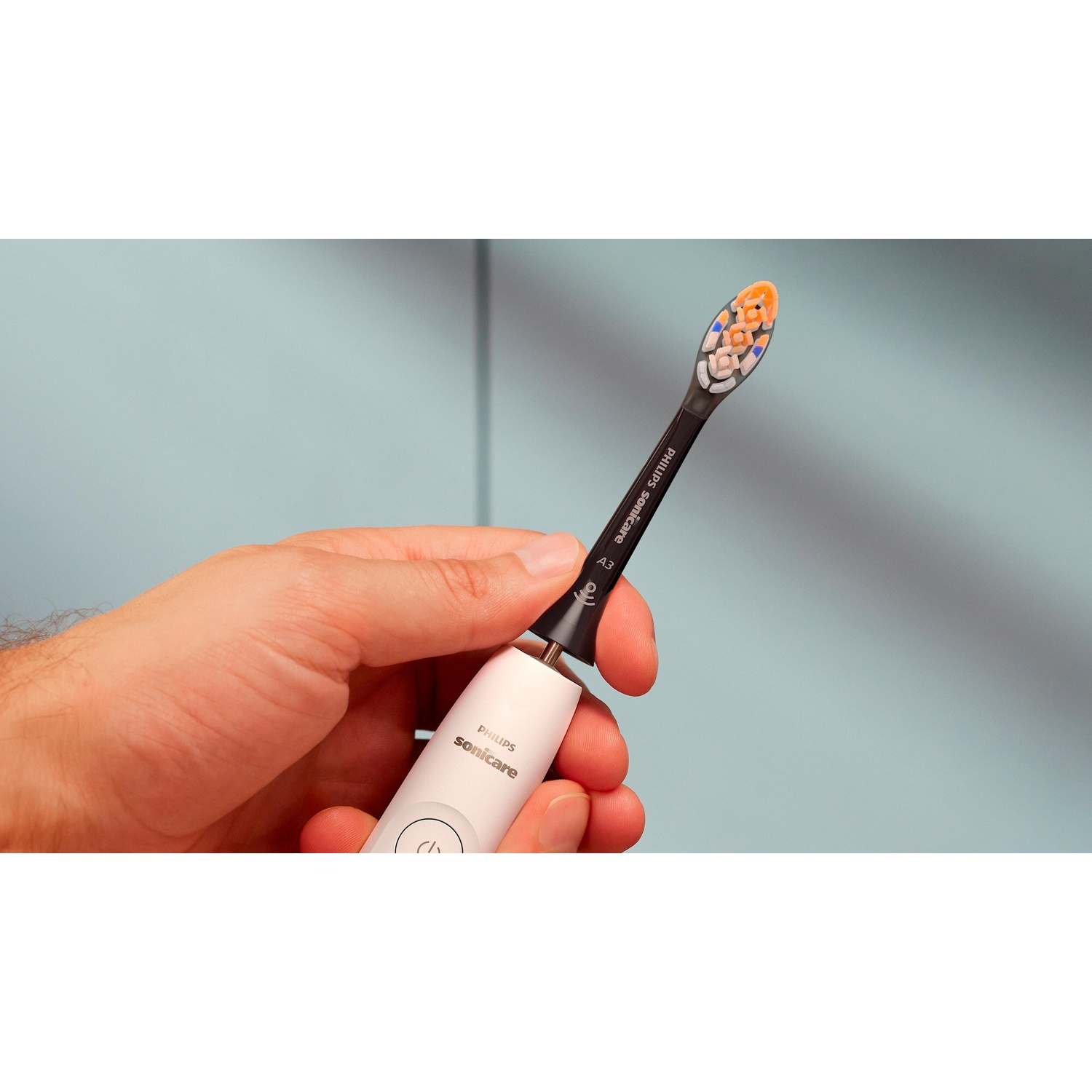 Hand holding a toothbrush. The brush head has orange, blue, and white bristles. Blue background.