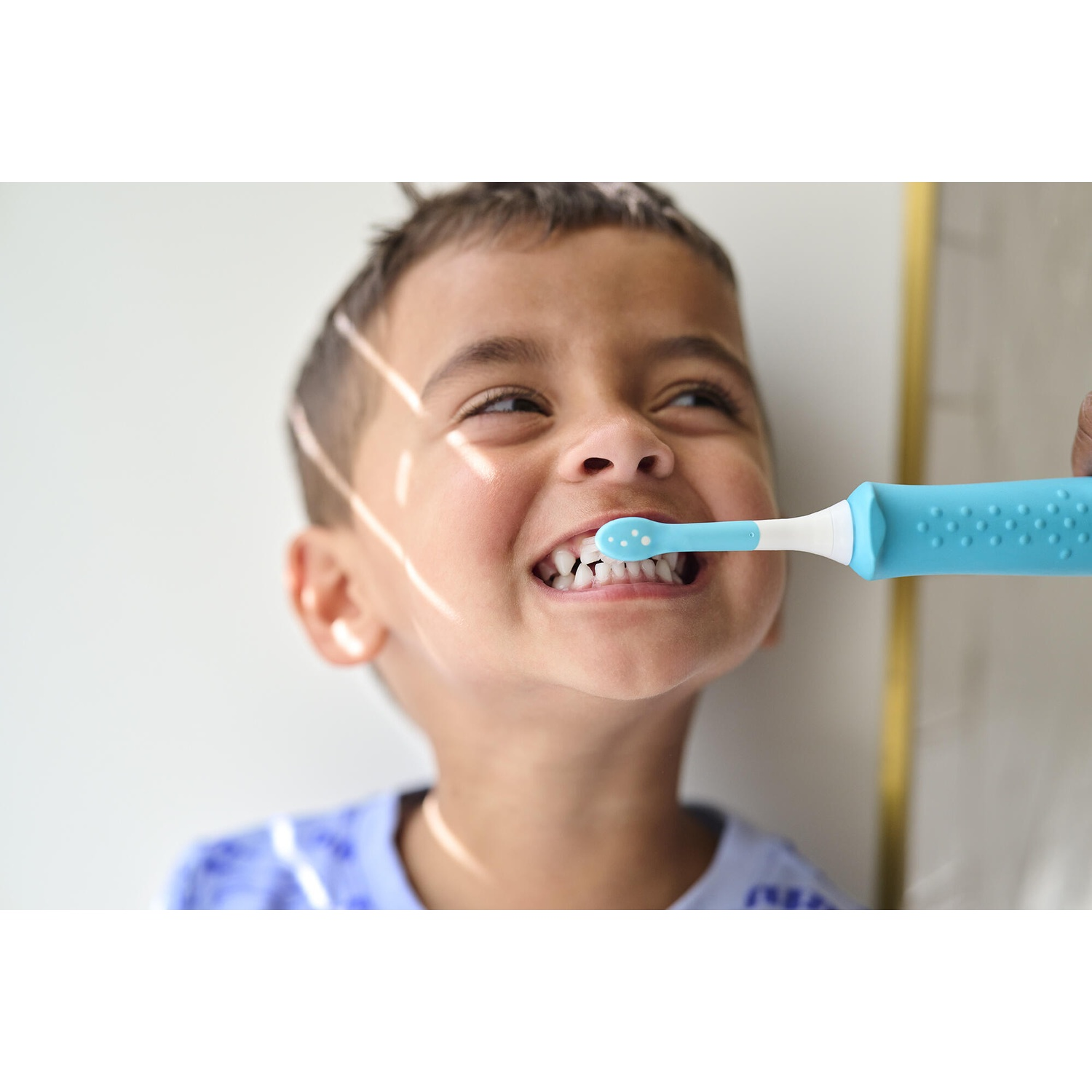Boy brushing teeth. Blue toothbrush and smiling boy. White teeth visible. Happy child.