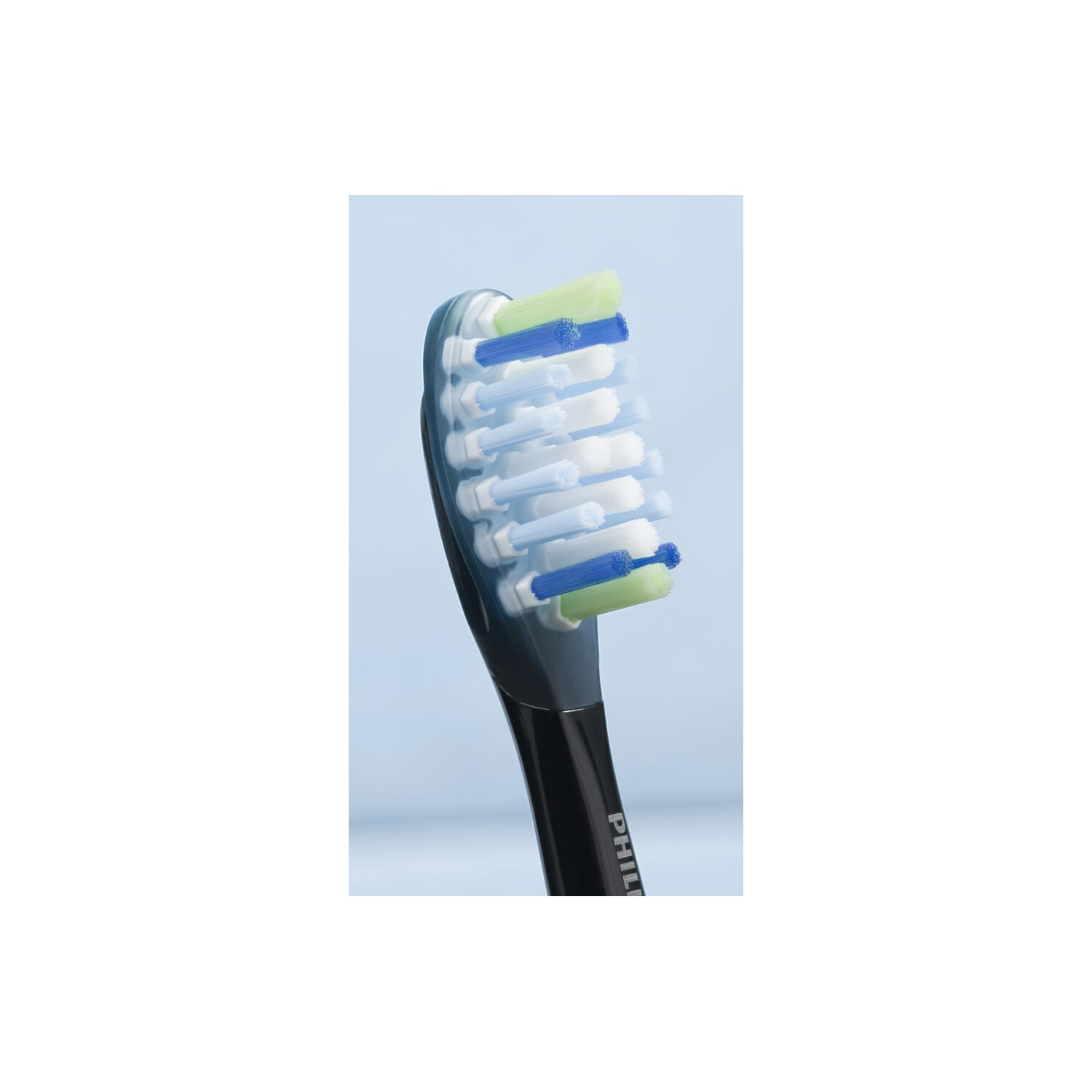 A close-up of a toothbrush head with blue, white, and green bristles against a light blue background.
