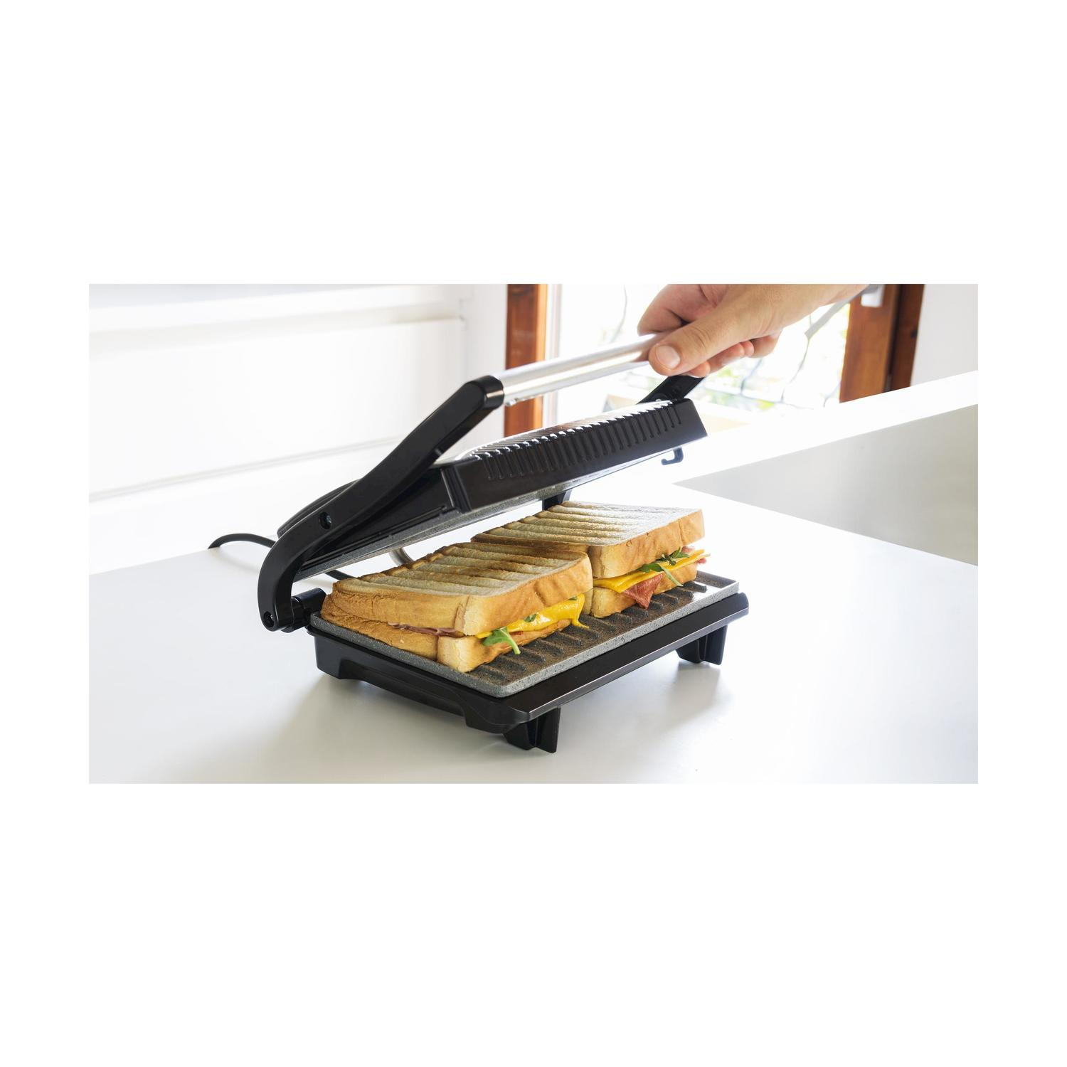 Pressa per panini nera con due panini all'interno, mano che tiene la maniglia.