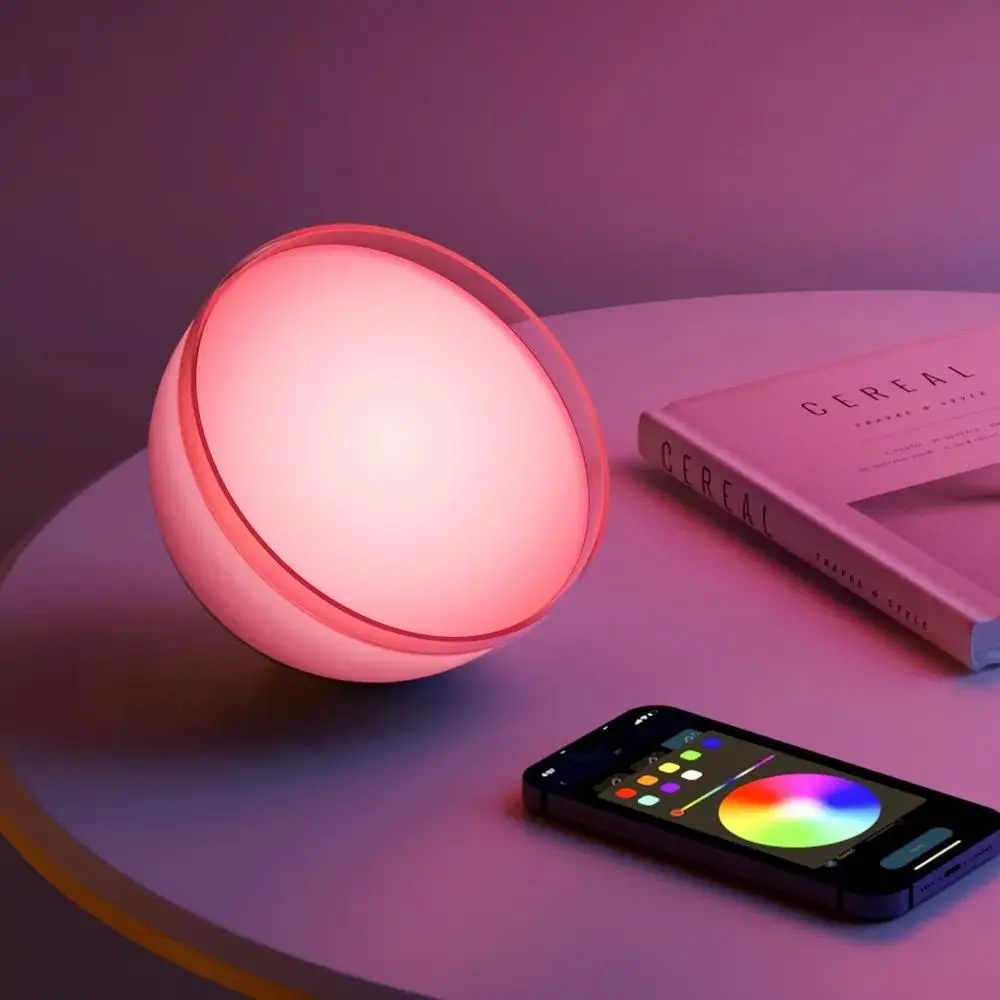 Okrągła, czerwono oświetlona lampa ze smartfonem. Książka leży na fioletowej powierzchni.