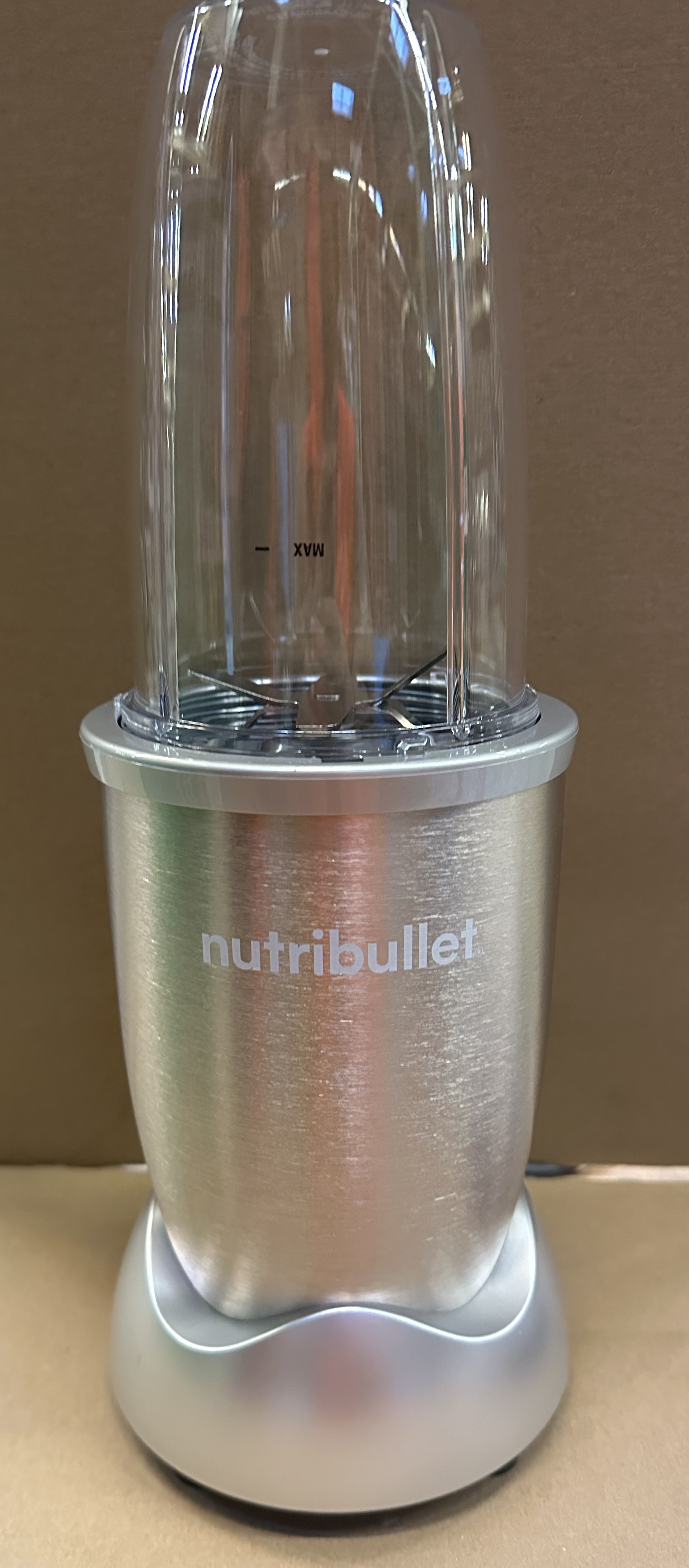 Blender Nutribullet ze srebrną podstawą i przezroczystym plastikowym pojemnikiem na górze.