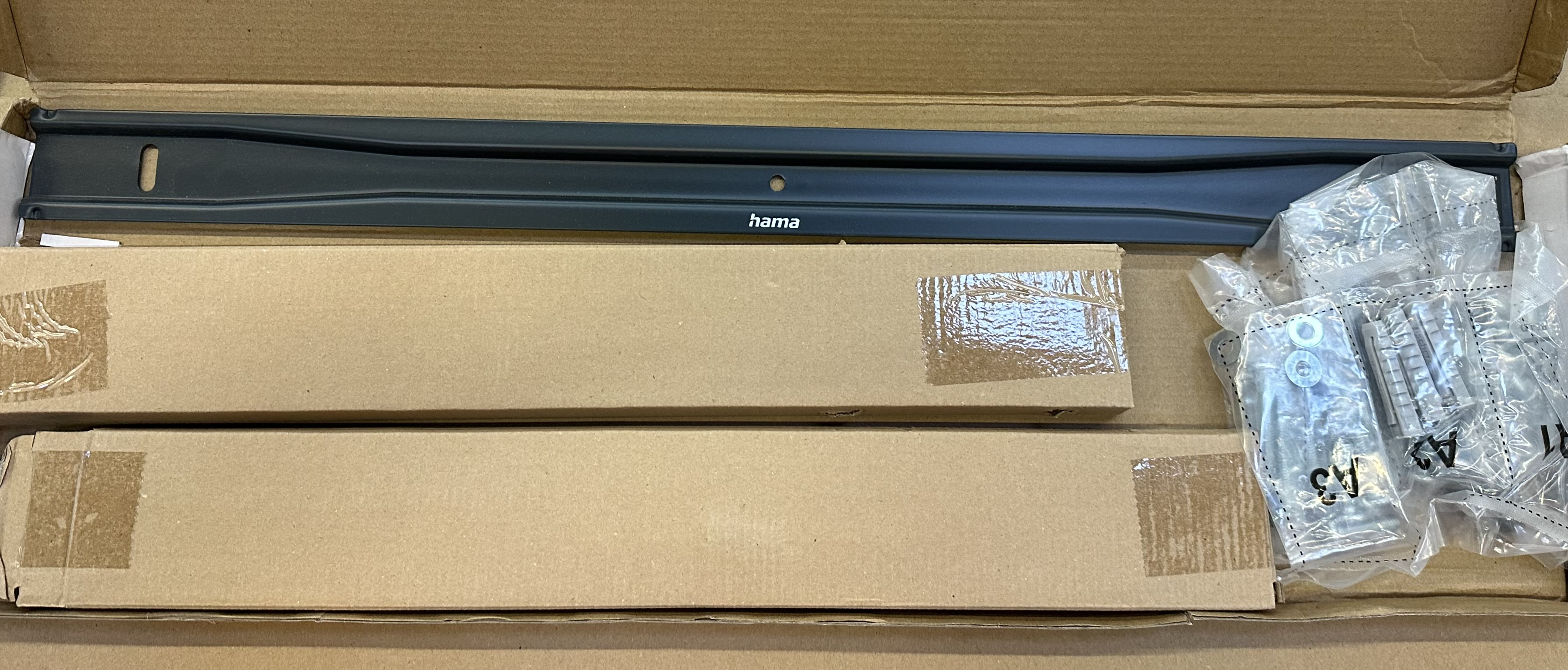 Czarny metalowy pręt, dwa kartony i małe woreczki ze śrubami w dużym kartonie.