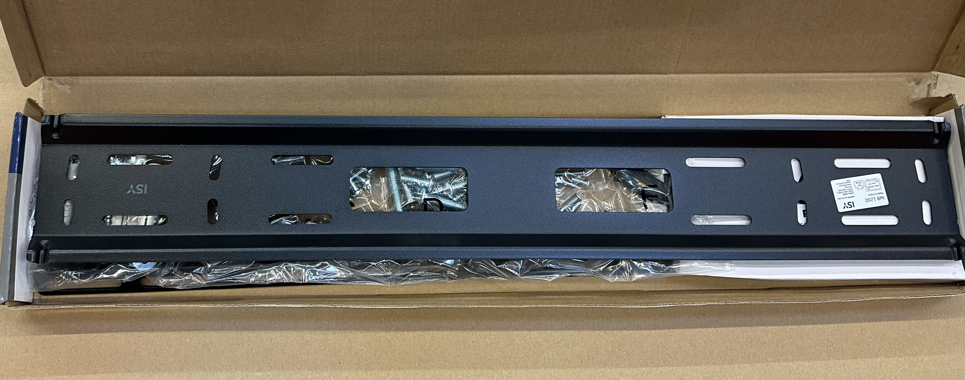 Czarny metalowy uchwyt do montażu telewizora w otwartym kartonie. Śruby widoczne wewnątrz pudełka.