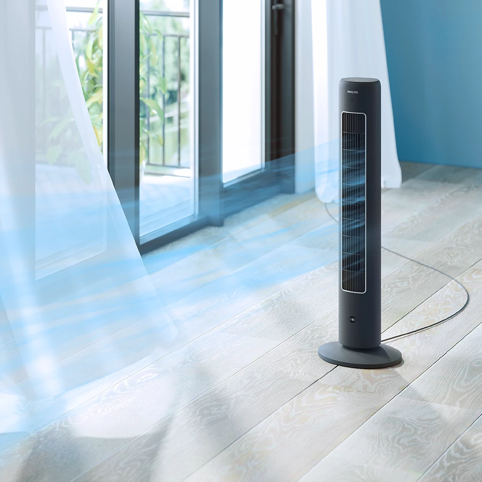 Un grand ventilateur Philips noir debout dans une pièce avec une fenêtre et un balcon visibles.