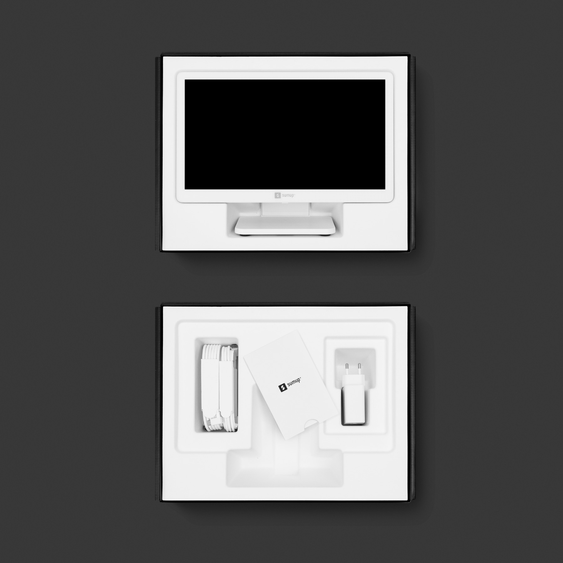 Tablette blanche, écran noir, dans une boîte ouverte. Chargeur et carte visibles.