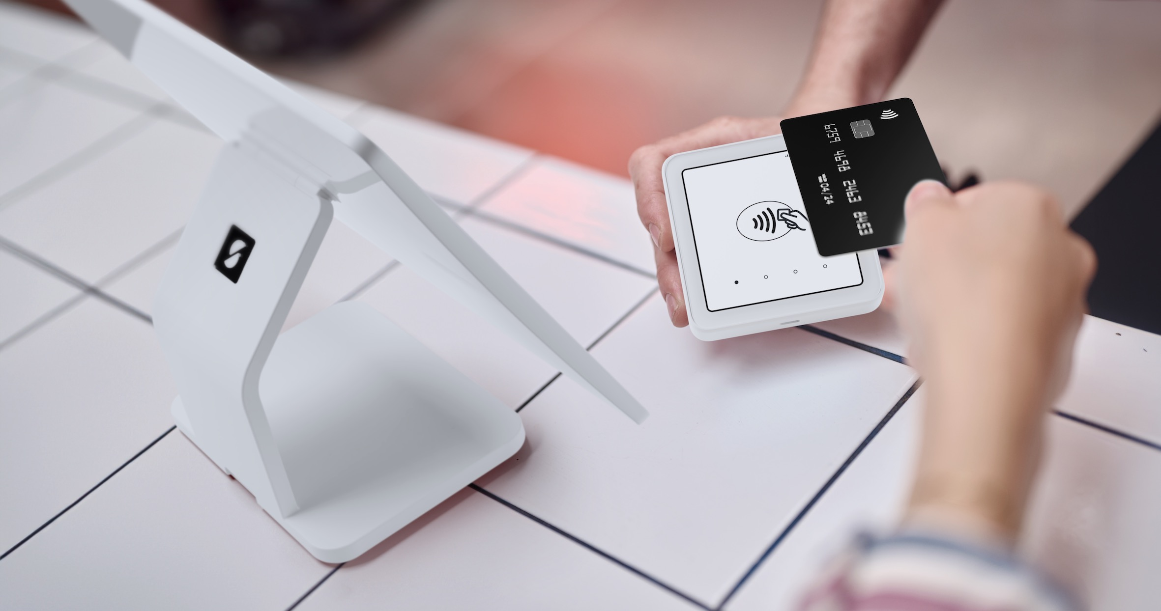 Personne payant avec une carte de crédit noire sur un système de point de vente blanc sur une surface blanche.