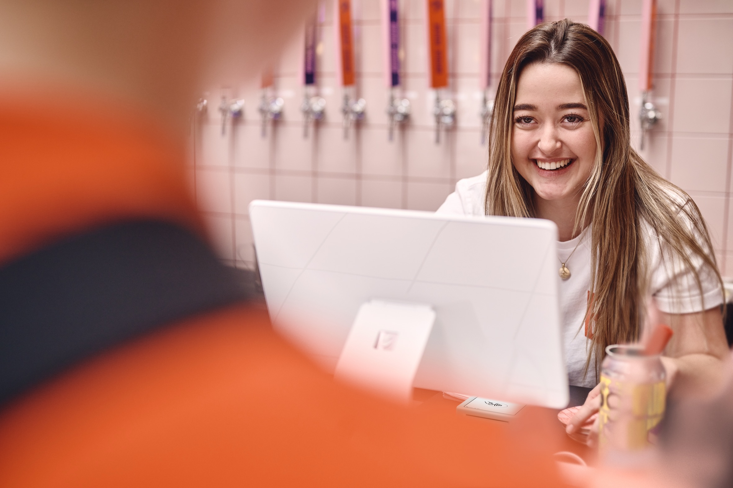 Femme souriant à un ordinateur au comptoir, avec des robinets en arrière-plan.