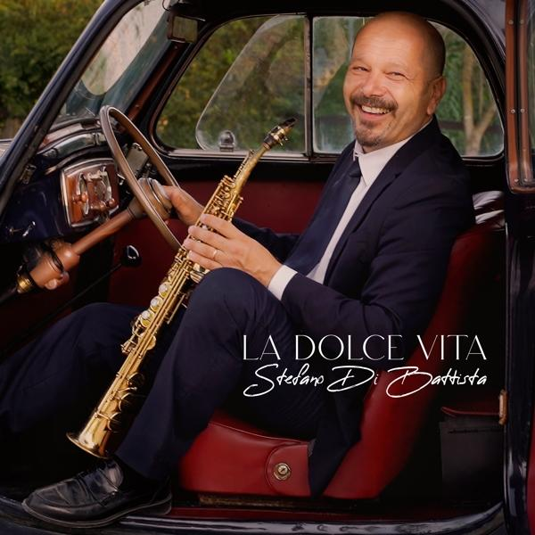 Egy férfi egy autóban szaxofonnal. A szöveg La Dolce Vita.