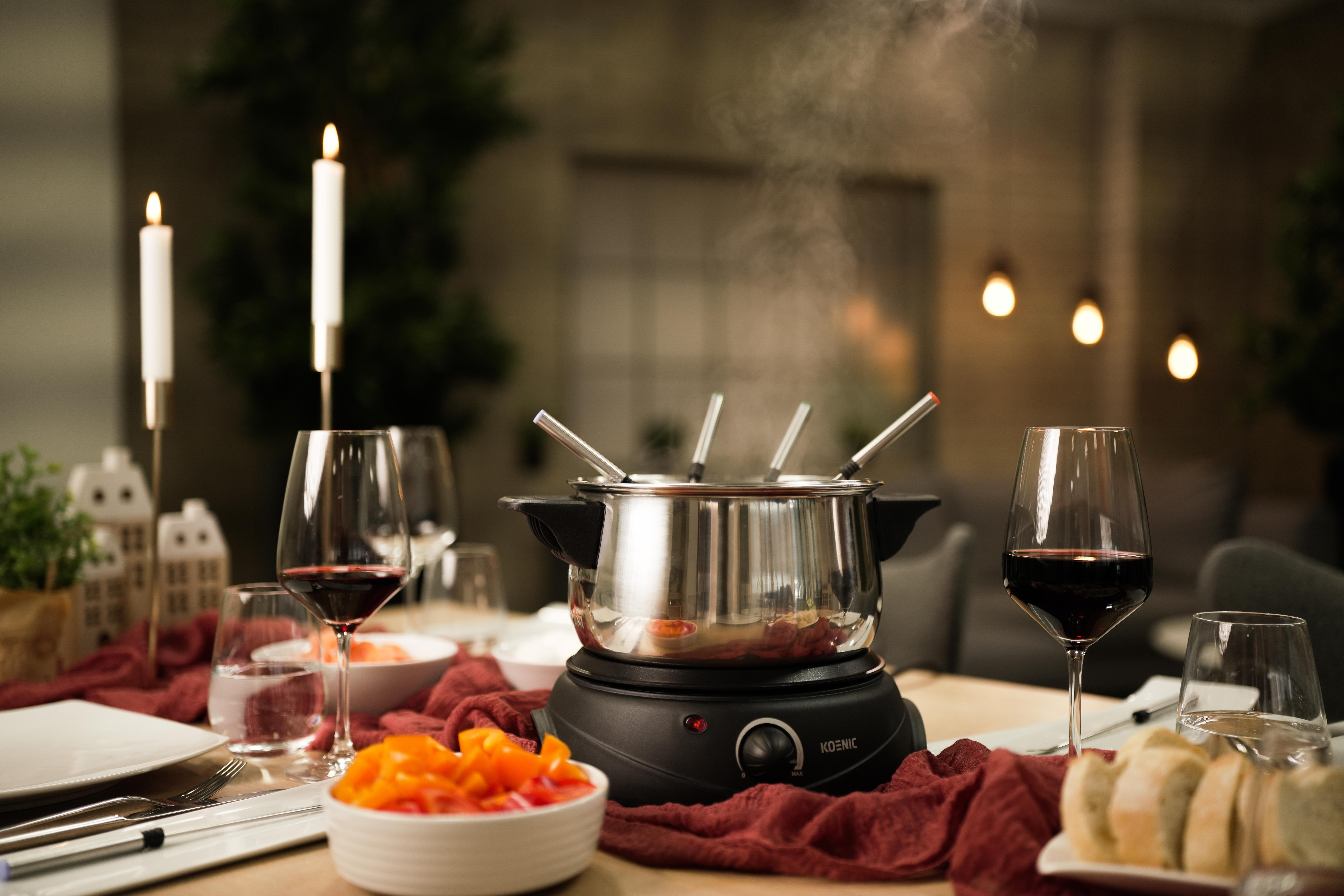 Ein Fonduetopf auf einem Tisch mit Weingläsern, Kerzen und einer Schüssel mit Gemüse.