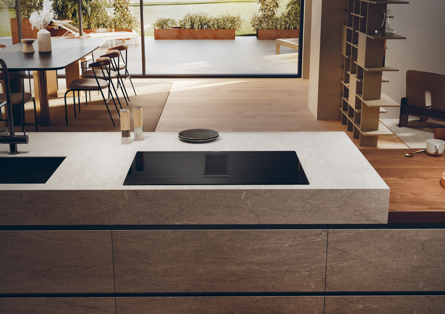 Escena de cocina con placa negra, extractor integrado y vista al jardín.