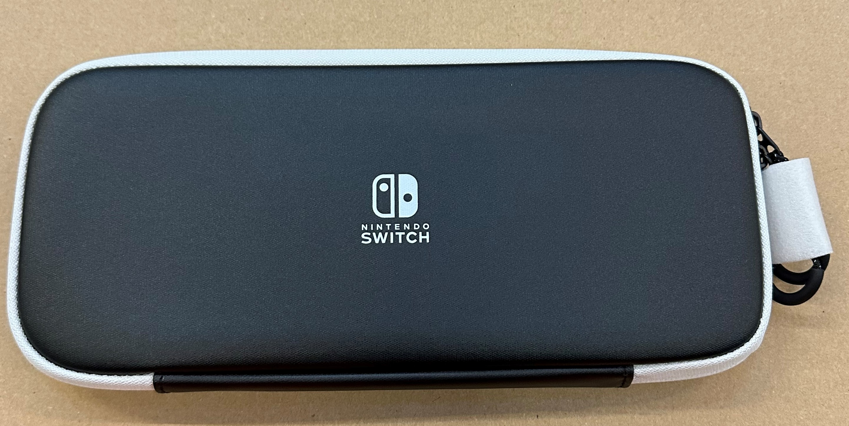 Czarny futerał Nintendo Switch z białym obramowaniem i logo na beżowej powierzchni.