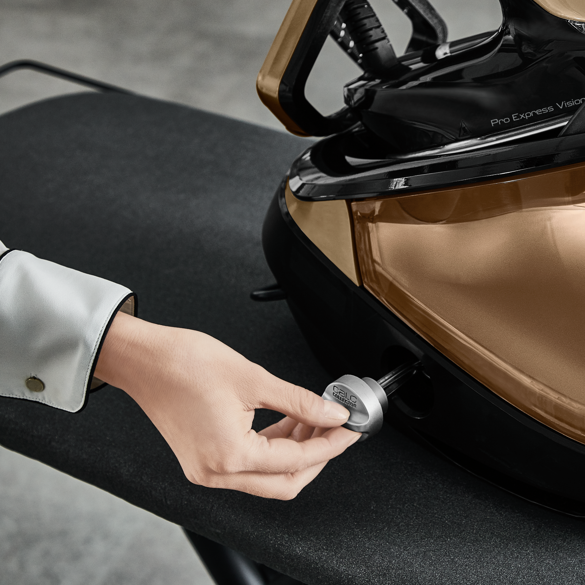 Ręka przekręca pokrętło na czarno-złotym żelazku, ustawionym na desce do prasowania.