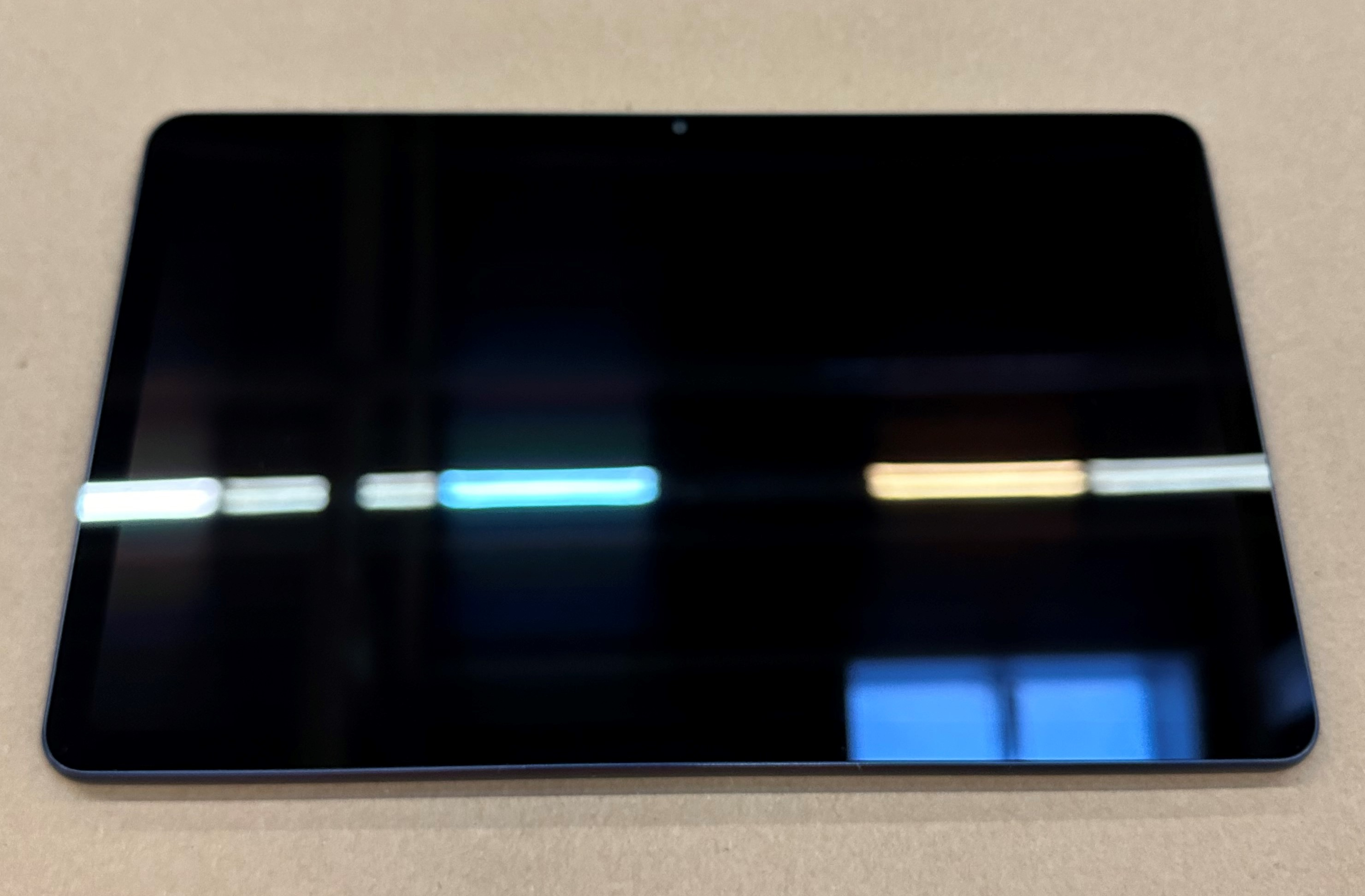 Czarny tablet na beżowej powierzchni. Światła odbijają się na ekranie.