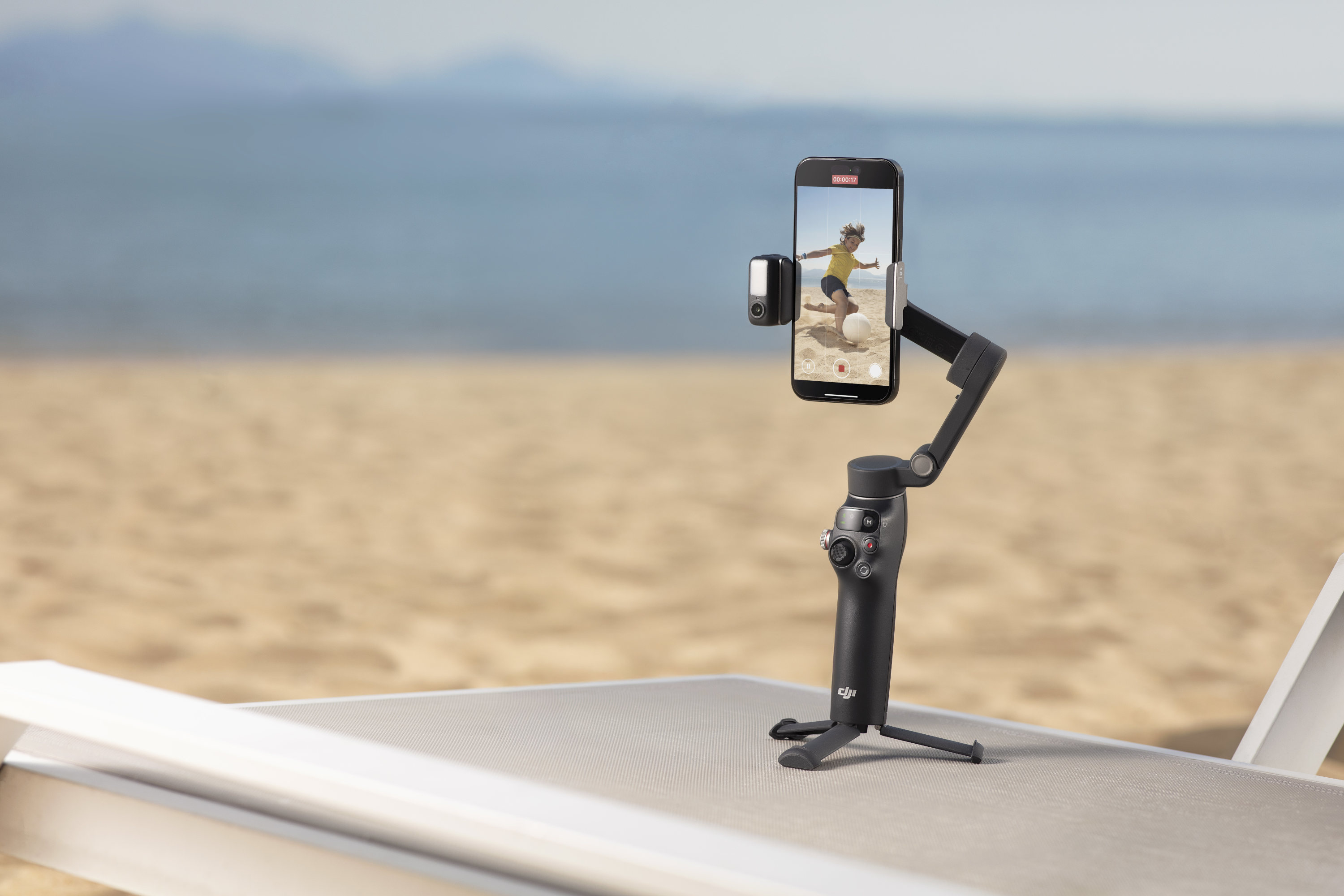 Un téléphone sur un trépied enregistre une fille sur la plage. L'arrière-plan est une plage et la mer.