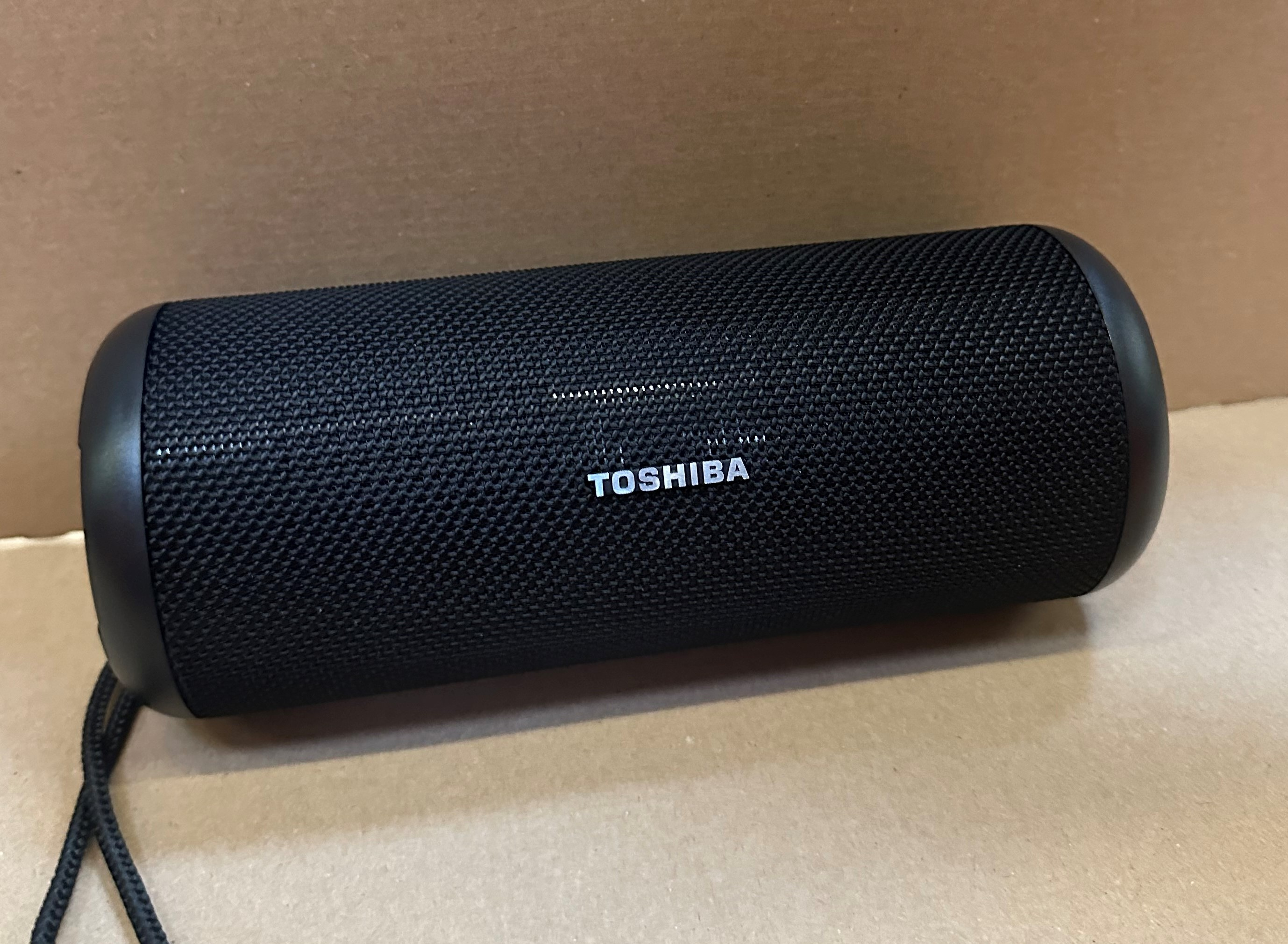 Czarny głośnik Toshiba na brązowej powierzchni, z widoczną nazwą marki.