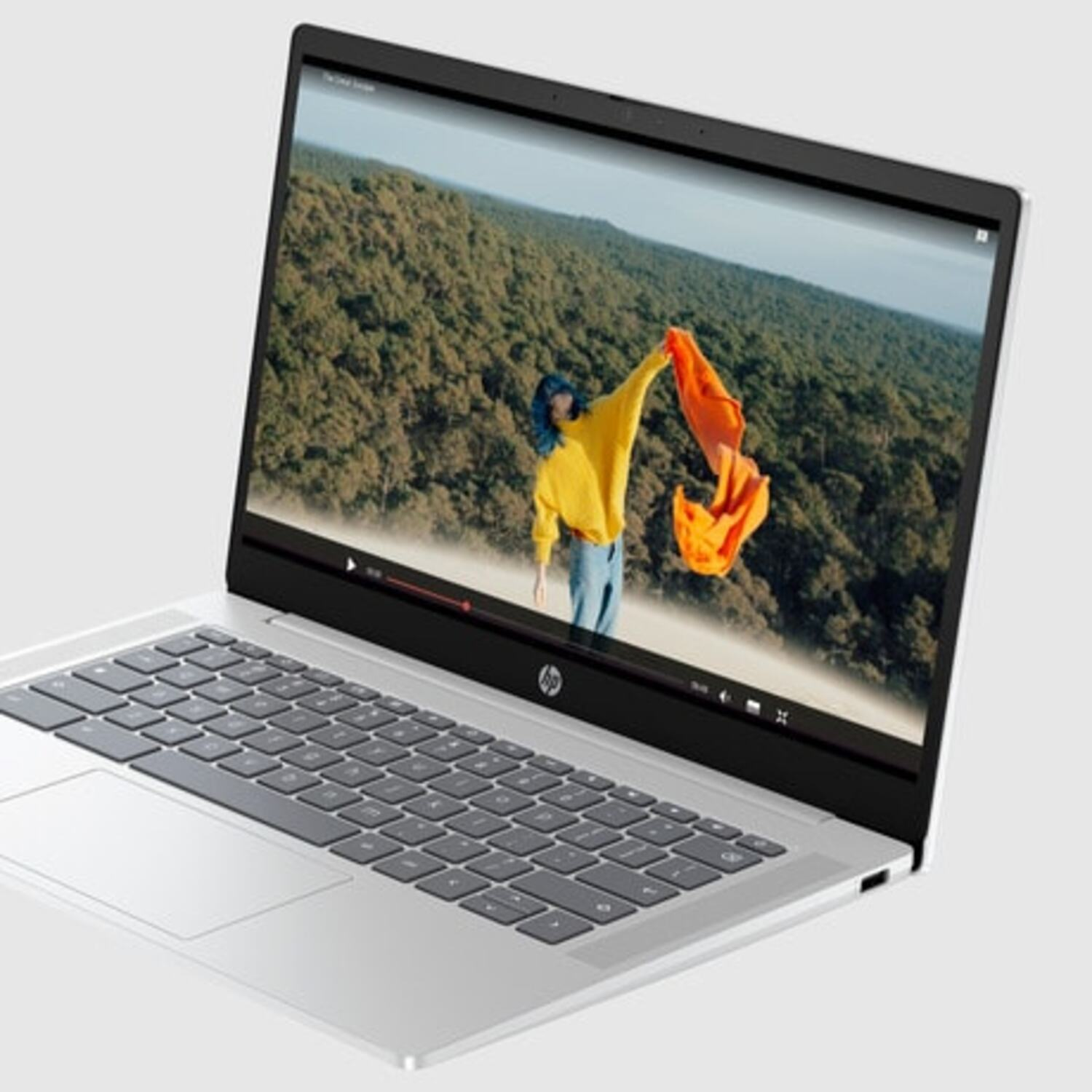 Silver laptop open, displaying a video. A person in yellow holds an orange scarf, trees in the background.