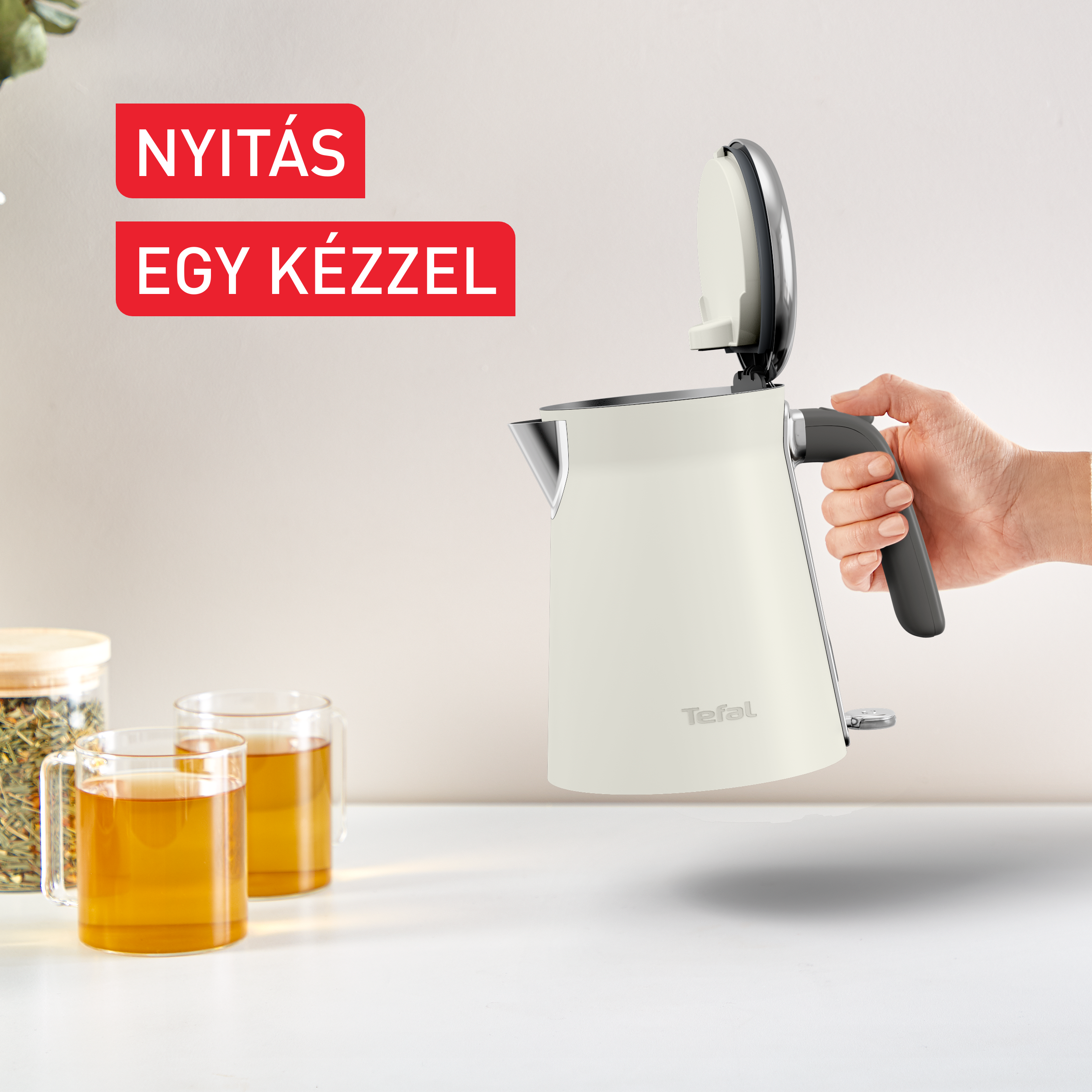 Egy fehér Tefal vízforraló nyitott fedéllel, kéz tartja.