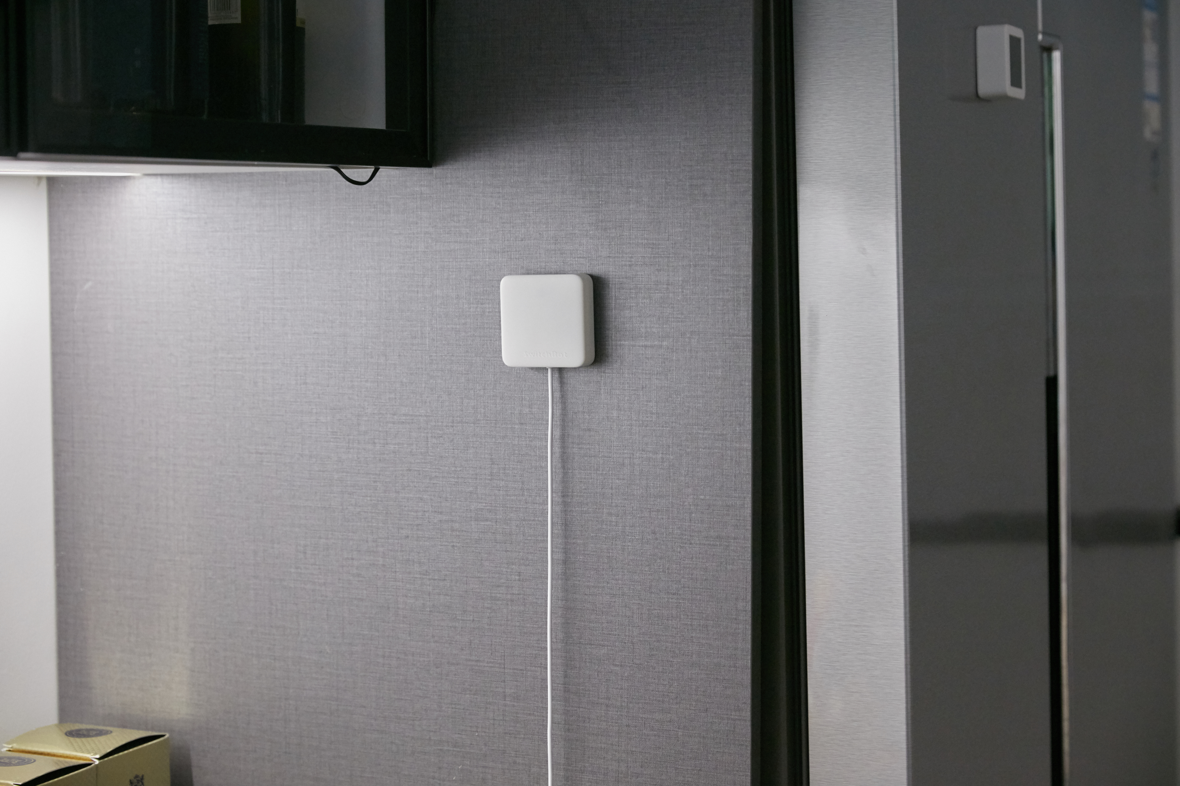 Ein weißes quadratisches Gerät an einer grauen Wand mit weißem Kabel.