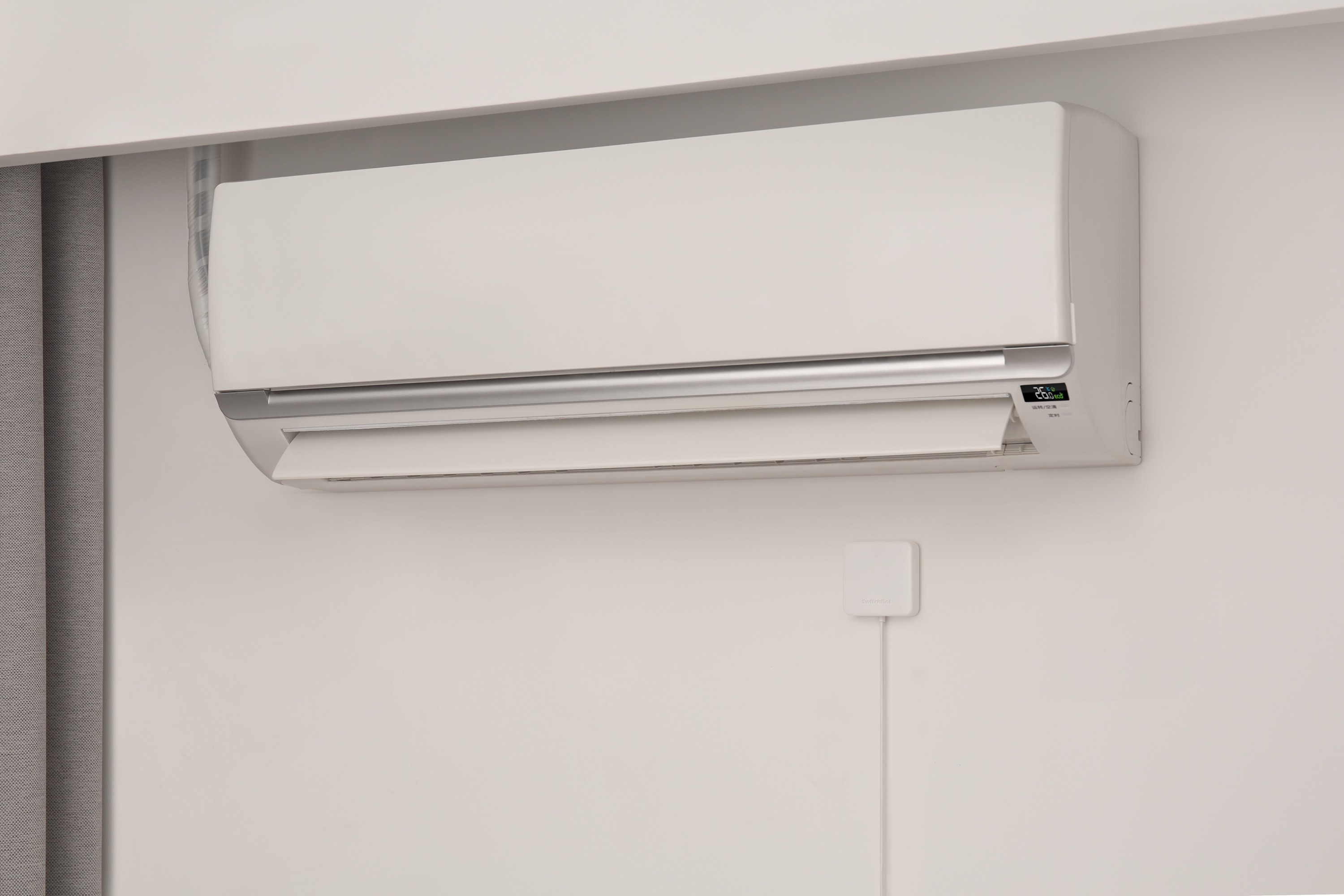Ein weißes Klimagerät ist an einer weißen Wand montiert. Darunter befindet sich eine kleine Box.