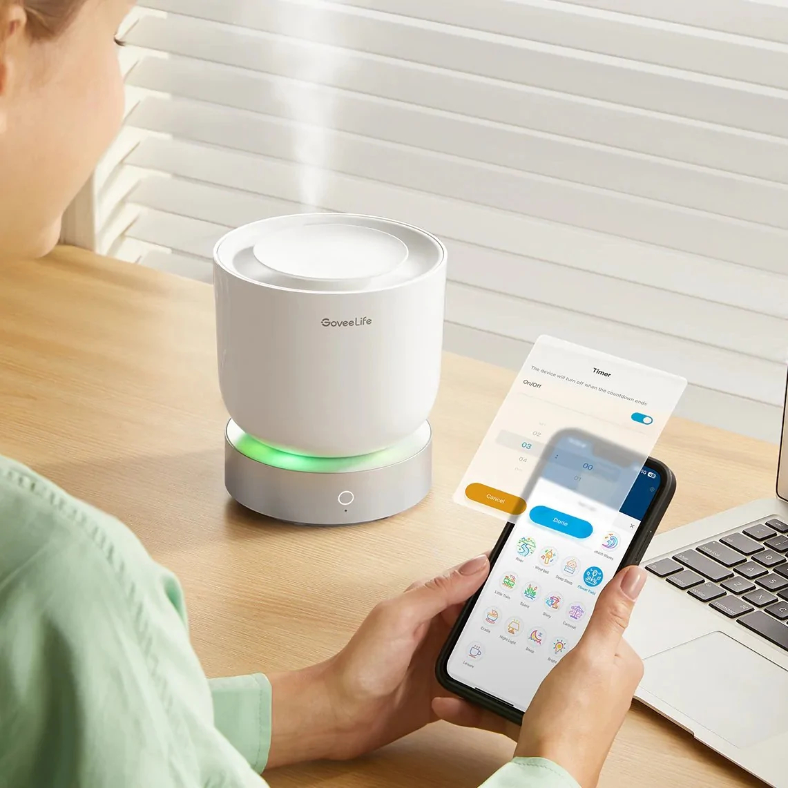 Kobieta używa smartfona do sterowania nawilżaczem na stoliku nocnym z laptopem.