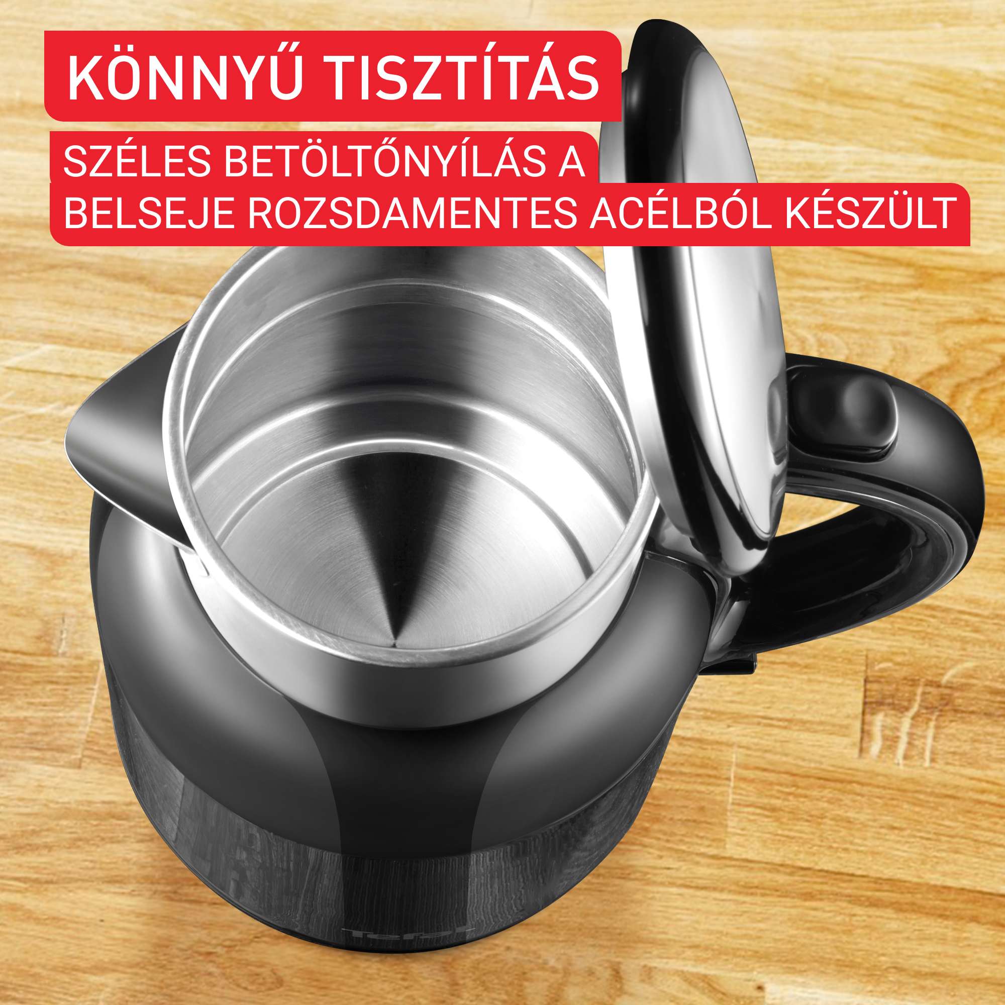 Nyitott fekete vízforraló ezüst belsővel, faerezetes felületen.