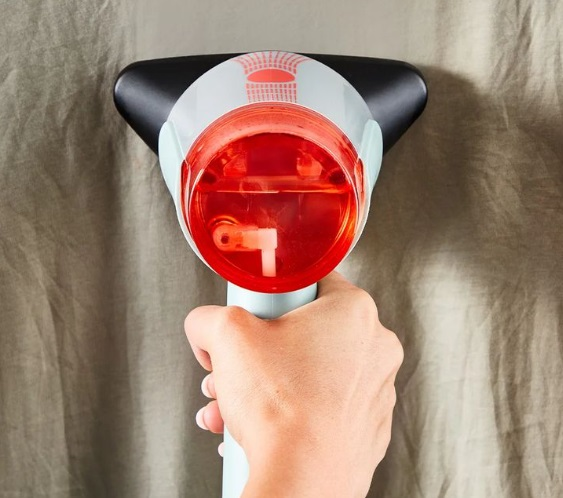 Ręka trzyma parownicę do tkanin nad materiałem.