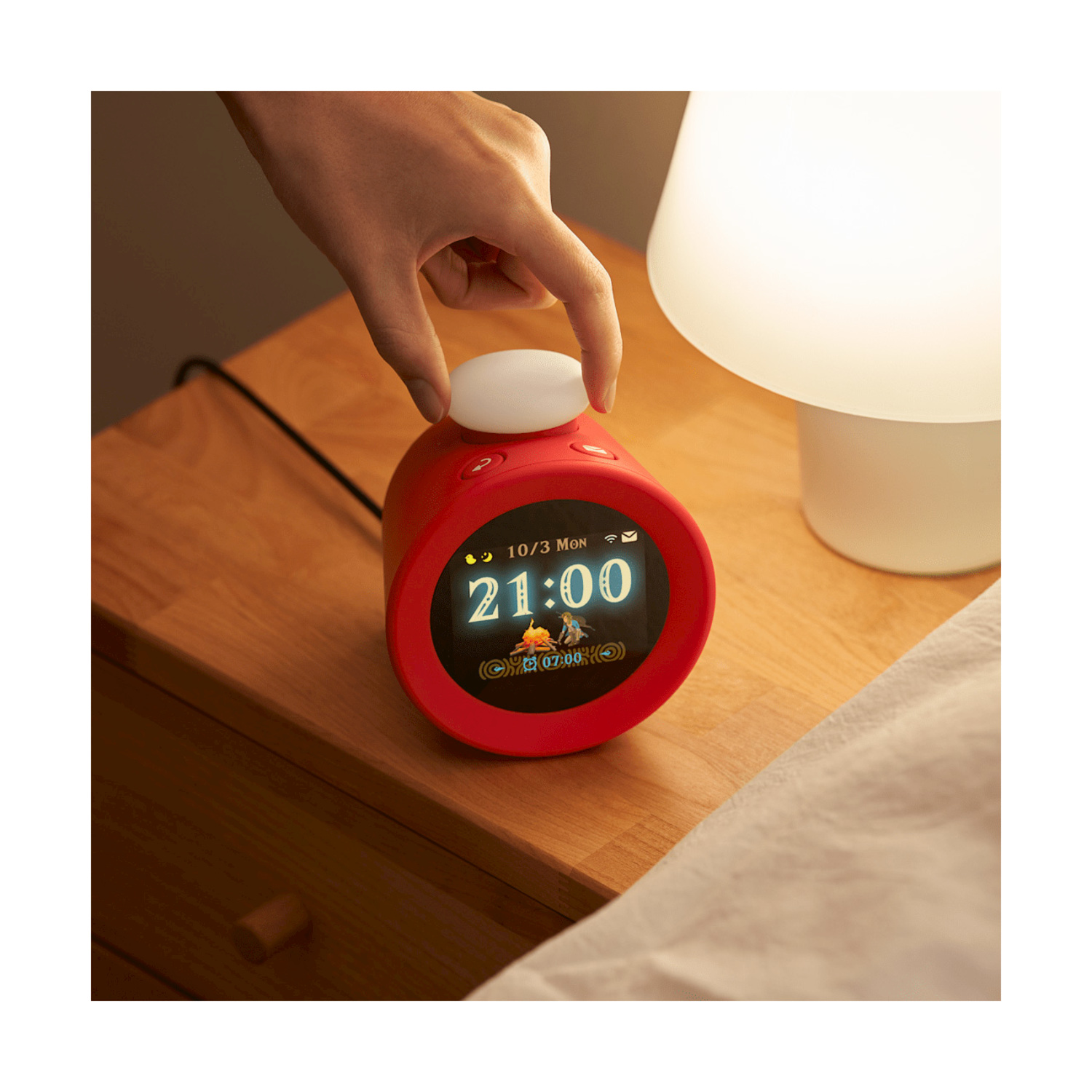 Una sveglia rossa su un comodino di legno. Una mano ruota il quadrante superiore. L'orologio segna le 21:00.