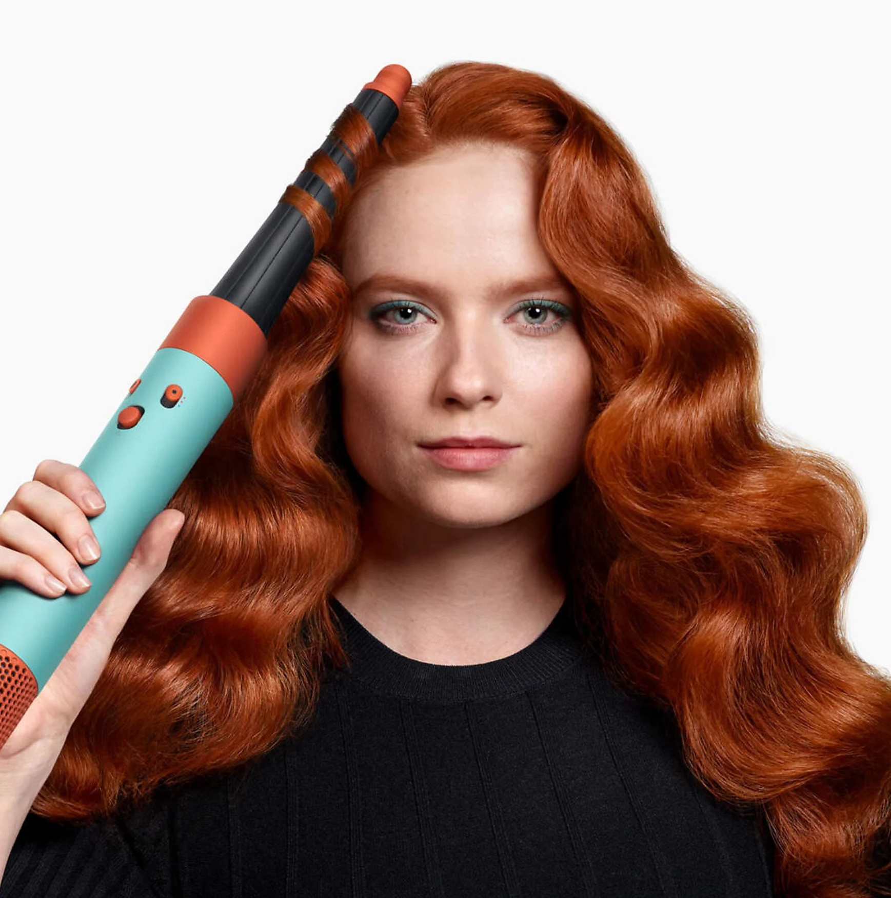 Kobieta z rudymi włosami trzyma lokówkę z turkusowym uchwytem.
