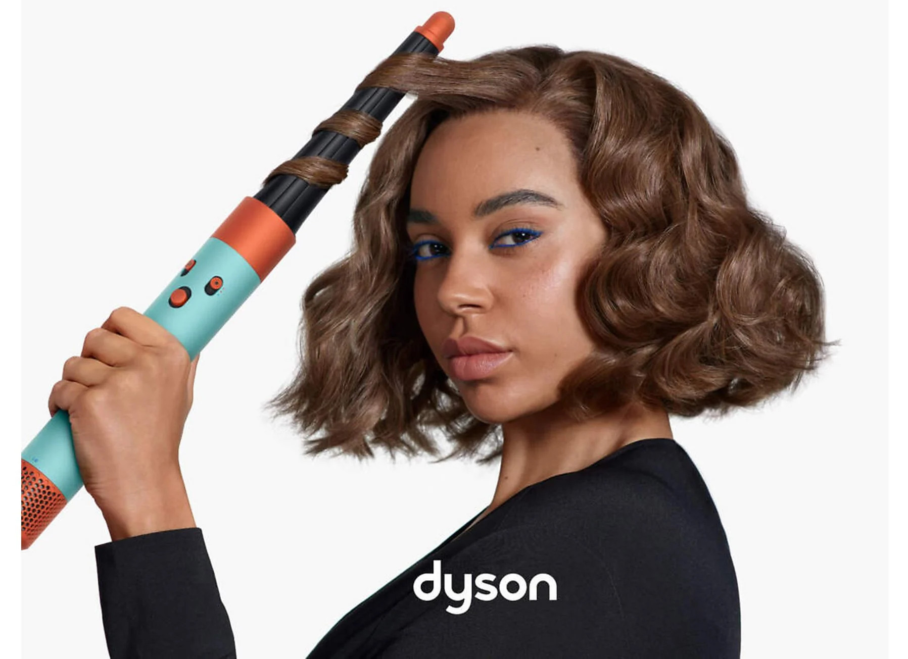 Kobieta z brązowymi lokami i niebieską lokówką Dyson.