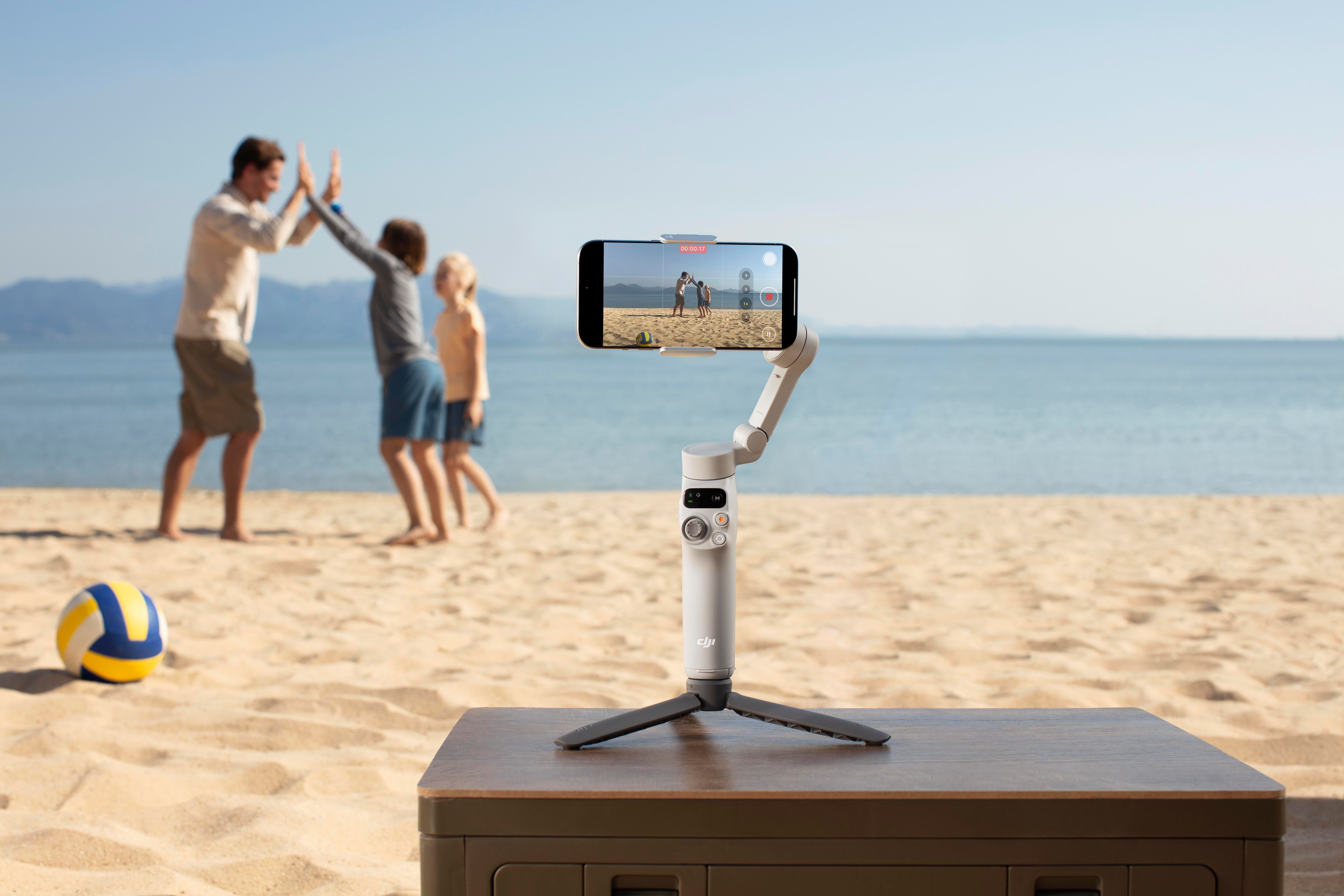 Strandszene: eine Familie gibt sich High-Five. Ein Videostabilisator steht auf einem Tisch, das Meer im Hintergrund.