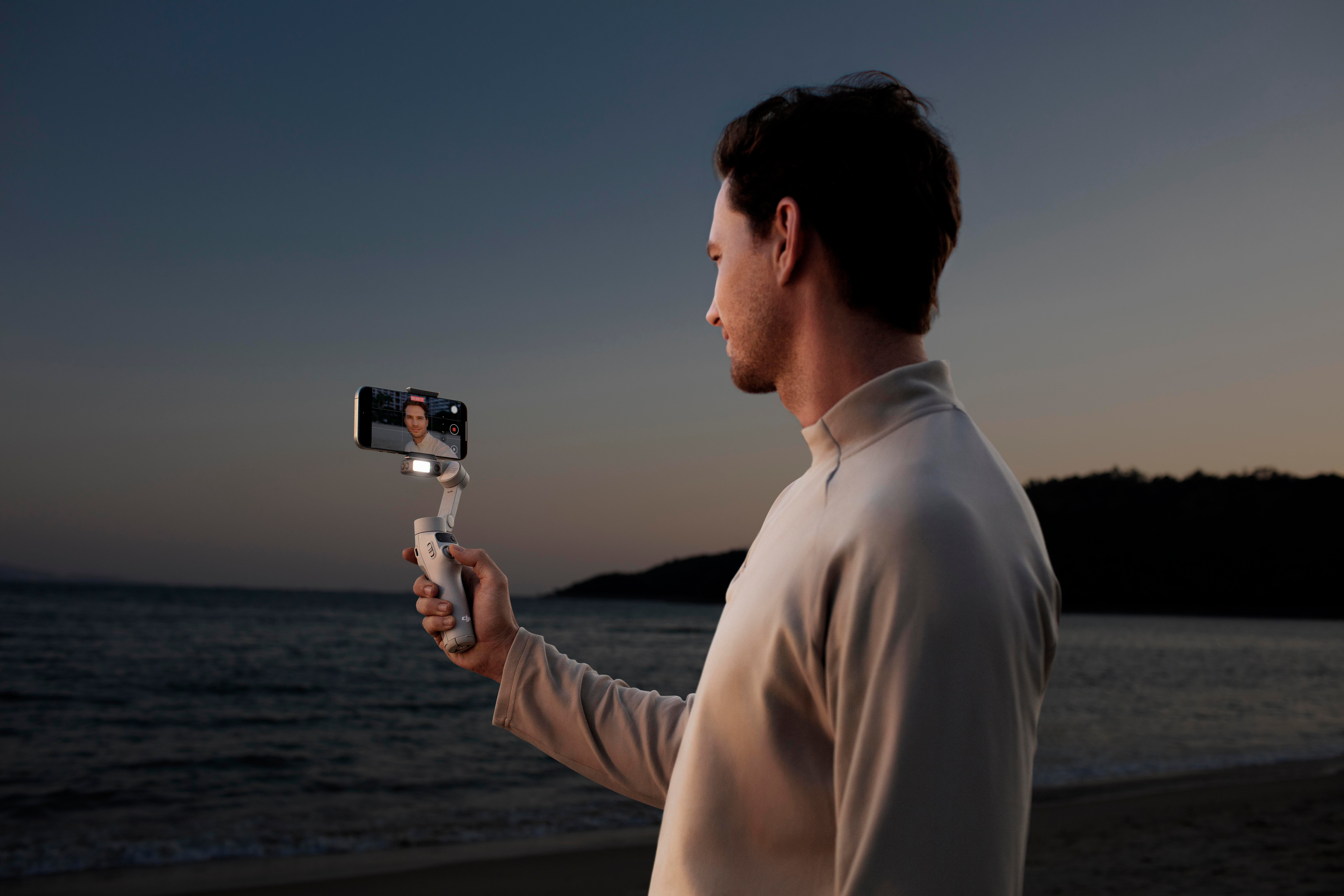 Mann hält Telefon mit Bildschirm am Strand, nutzt Handheld-Gimbal.