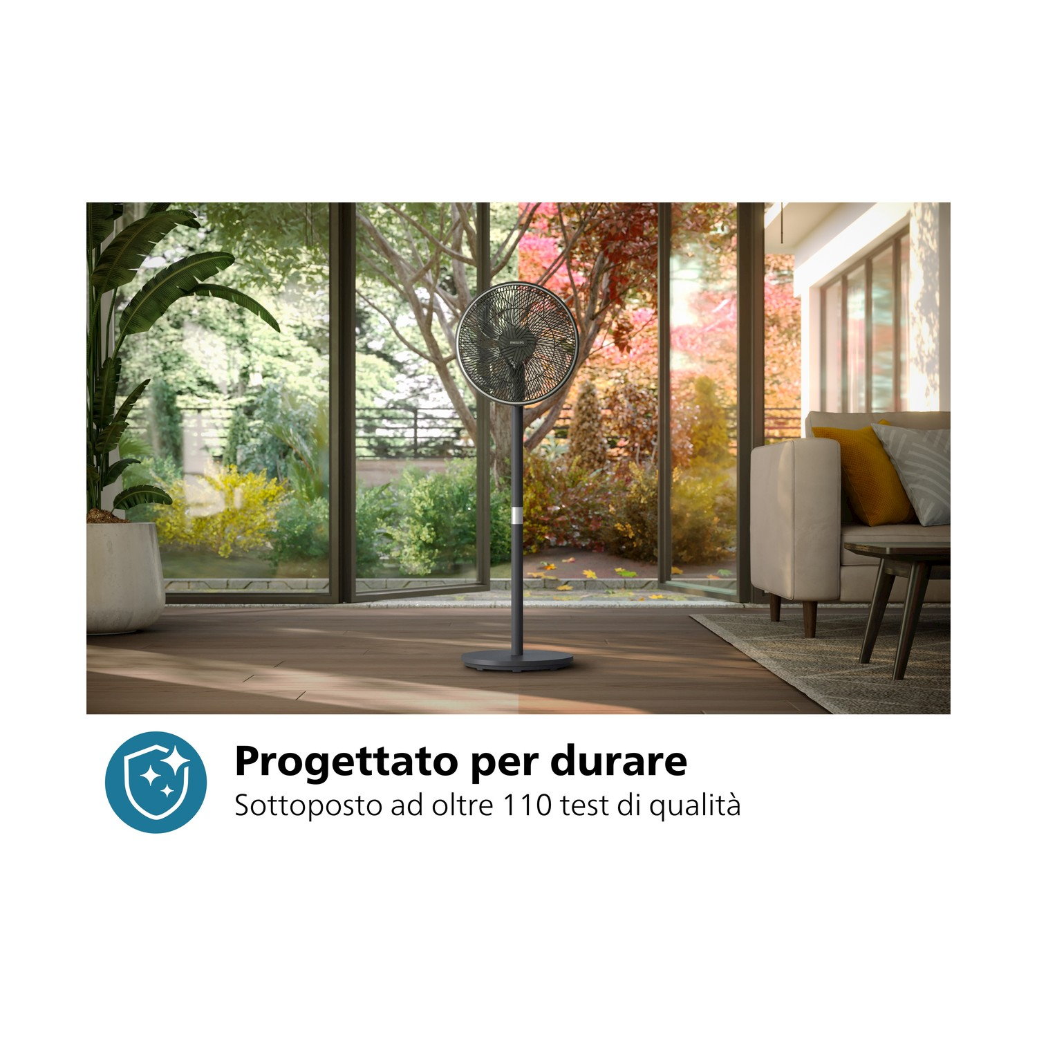 Ventilatore in una stanza; alberi attraverso la finestra, divano e tavolo visibili.